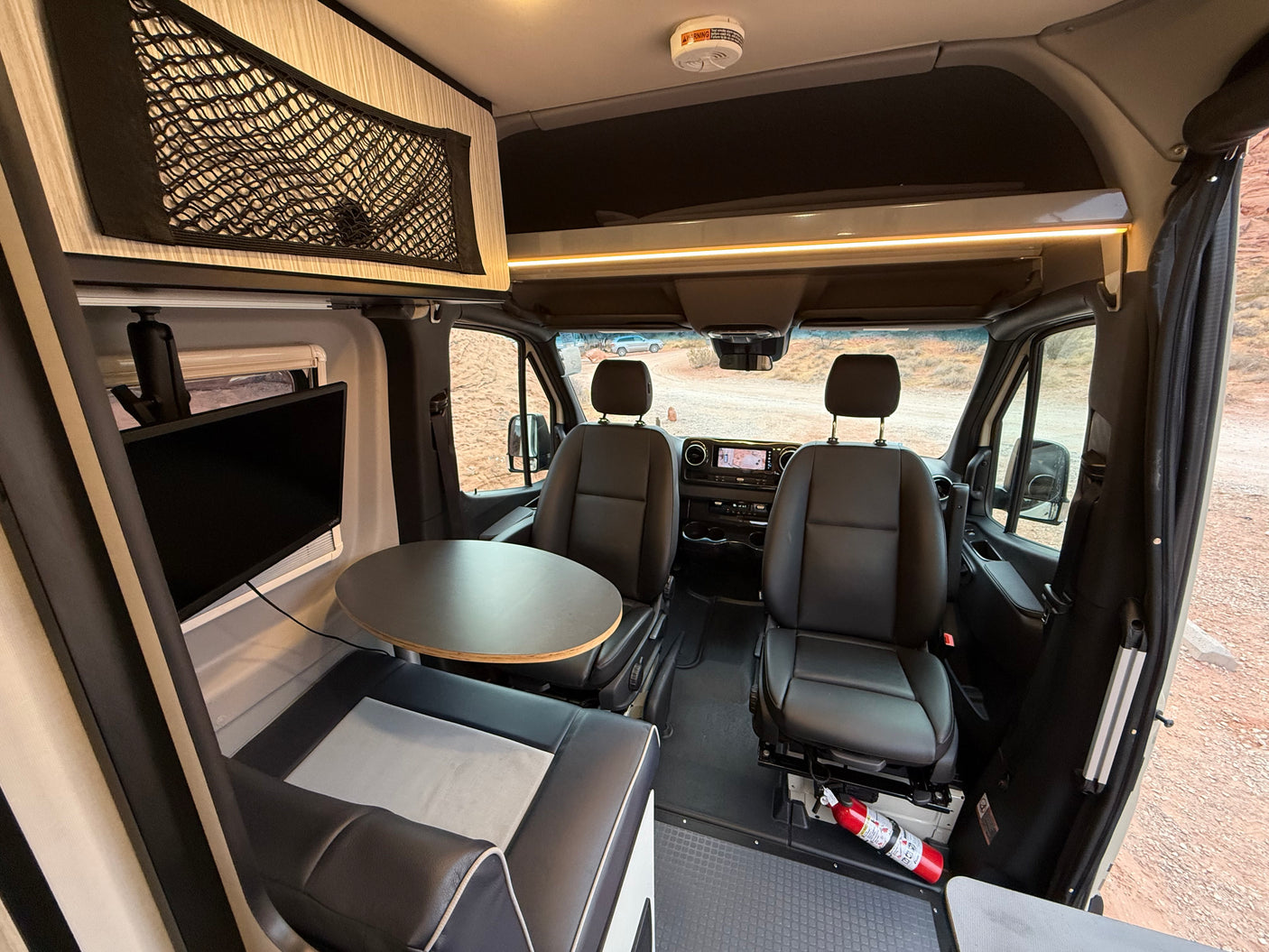 Comfortable RV rental interior: front cabin with swivel seats, dining area, TV, and overhead storage.