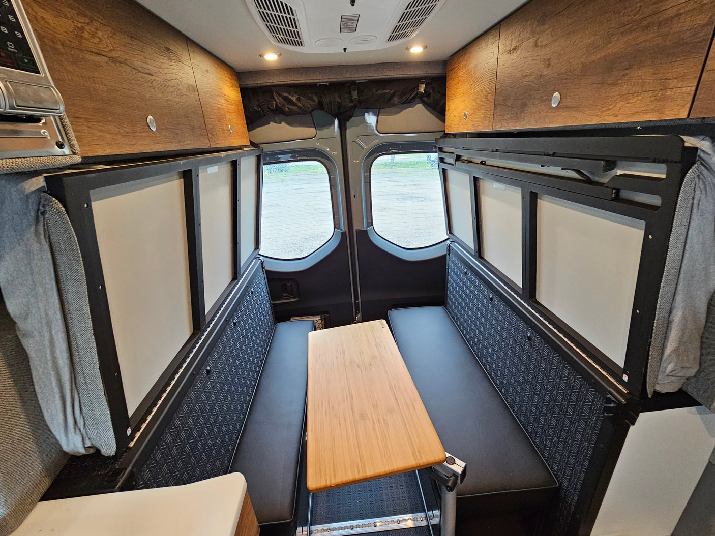 Inside this RV rental: a flexible camper van dinette/bed setup with benches, a table, wood cabinets, and rear windows.