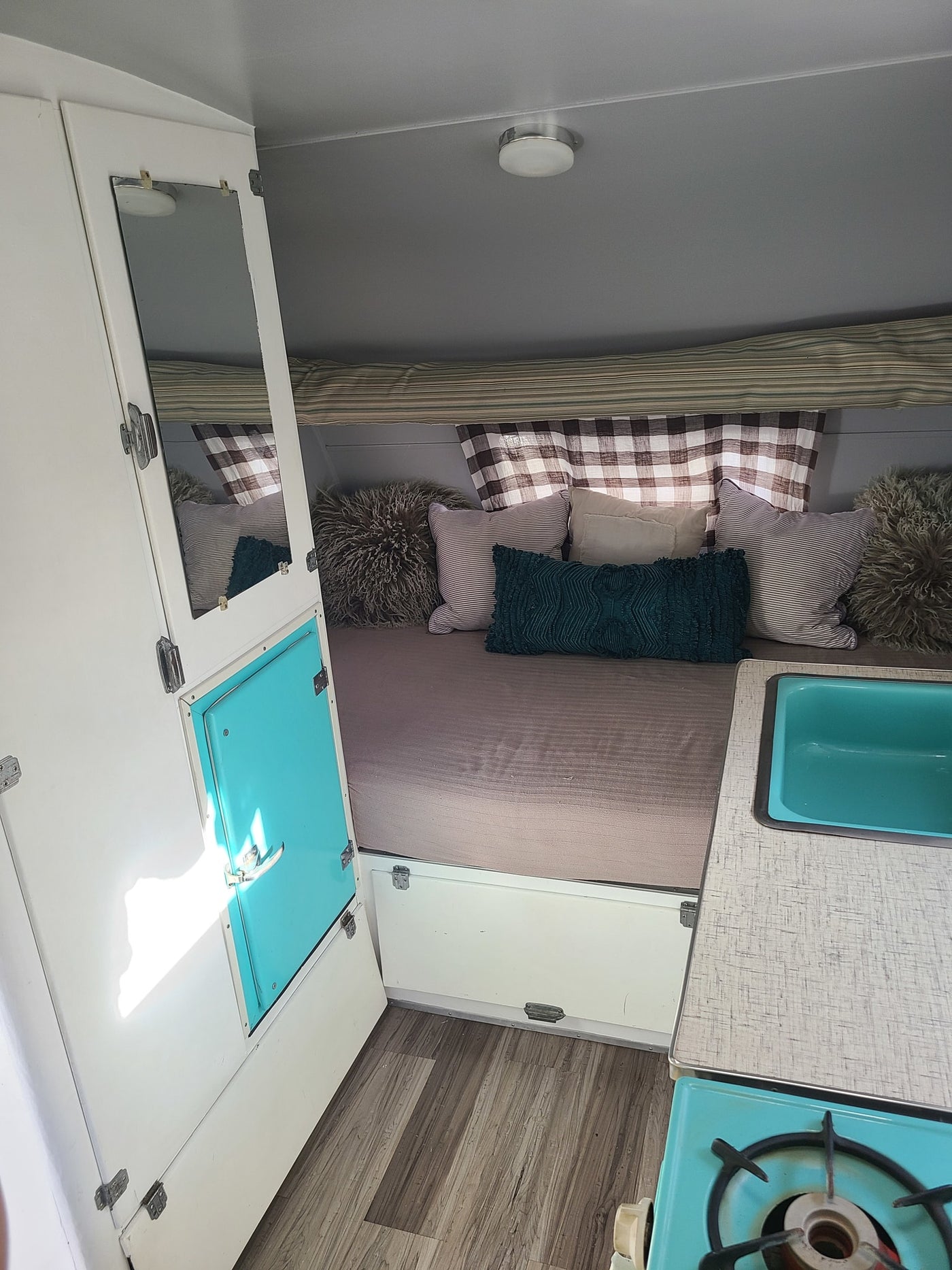 RV rental: Cozy camper interior, featuring a bed with pillows, teal sink, and stove setup. — photo 10