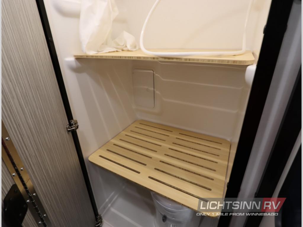 RV rental shower/bathroom with sleek wooden shelving & slatted floor mat. Practical design for travel comfort.
