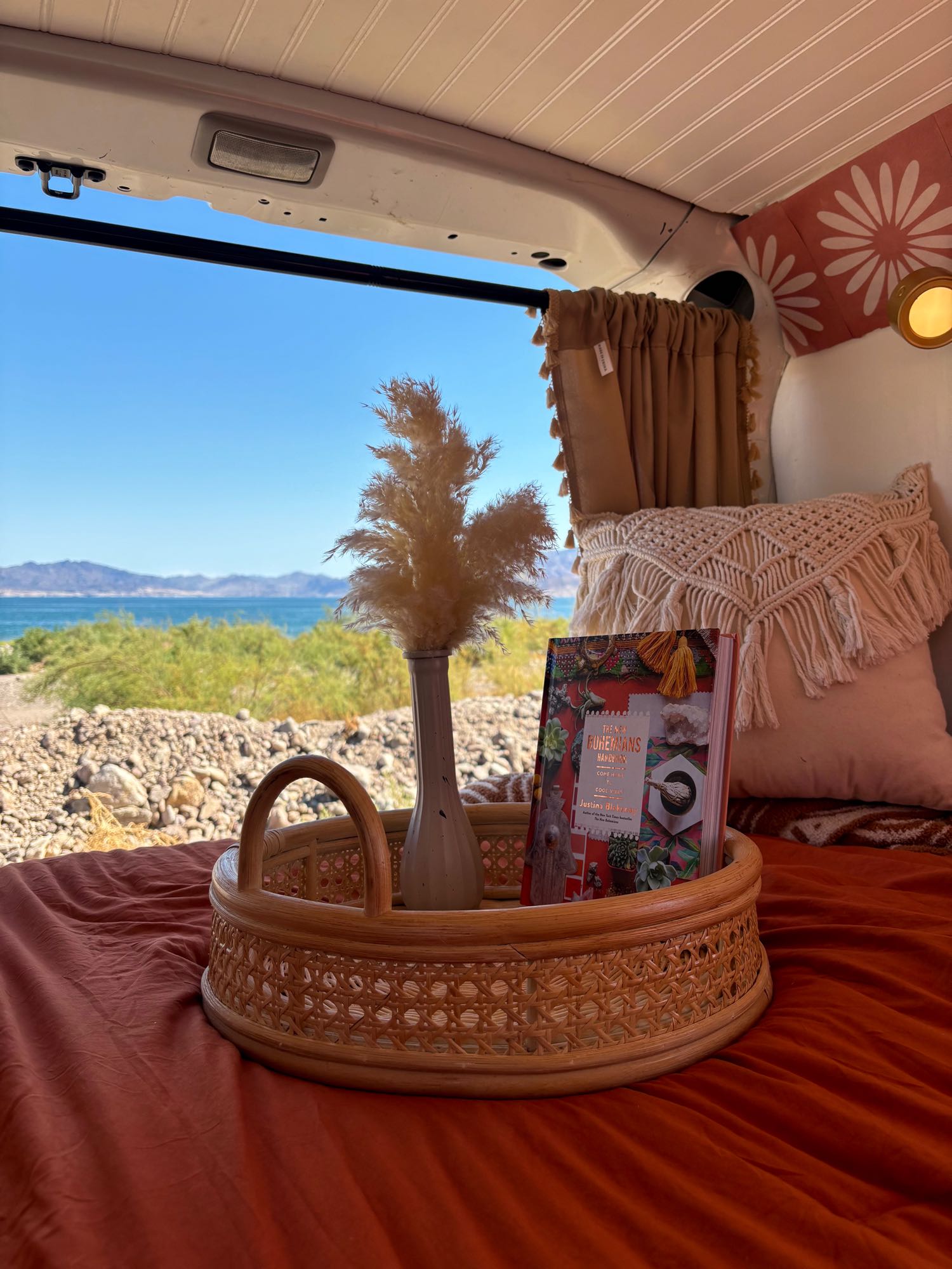 Cozy RV rental interior offers a serene lake view, perfect for van life adventures. Features a wicker tray with a book.