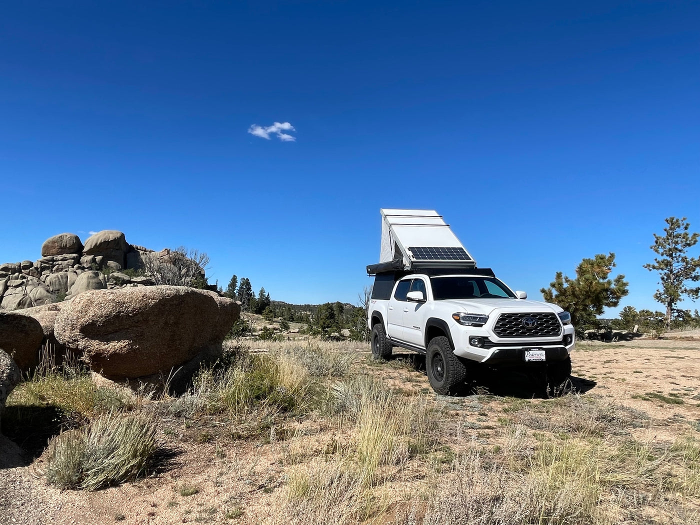 White Toyota Tacoma overland rig with pop-top camper and solar panels, perfect for an RV rental adventure in rocky terrain. — photo 6