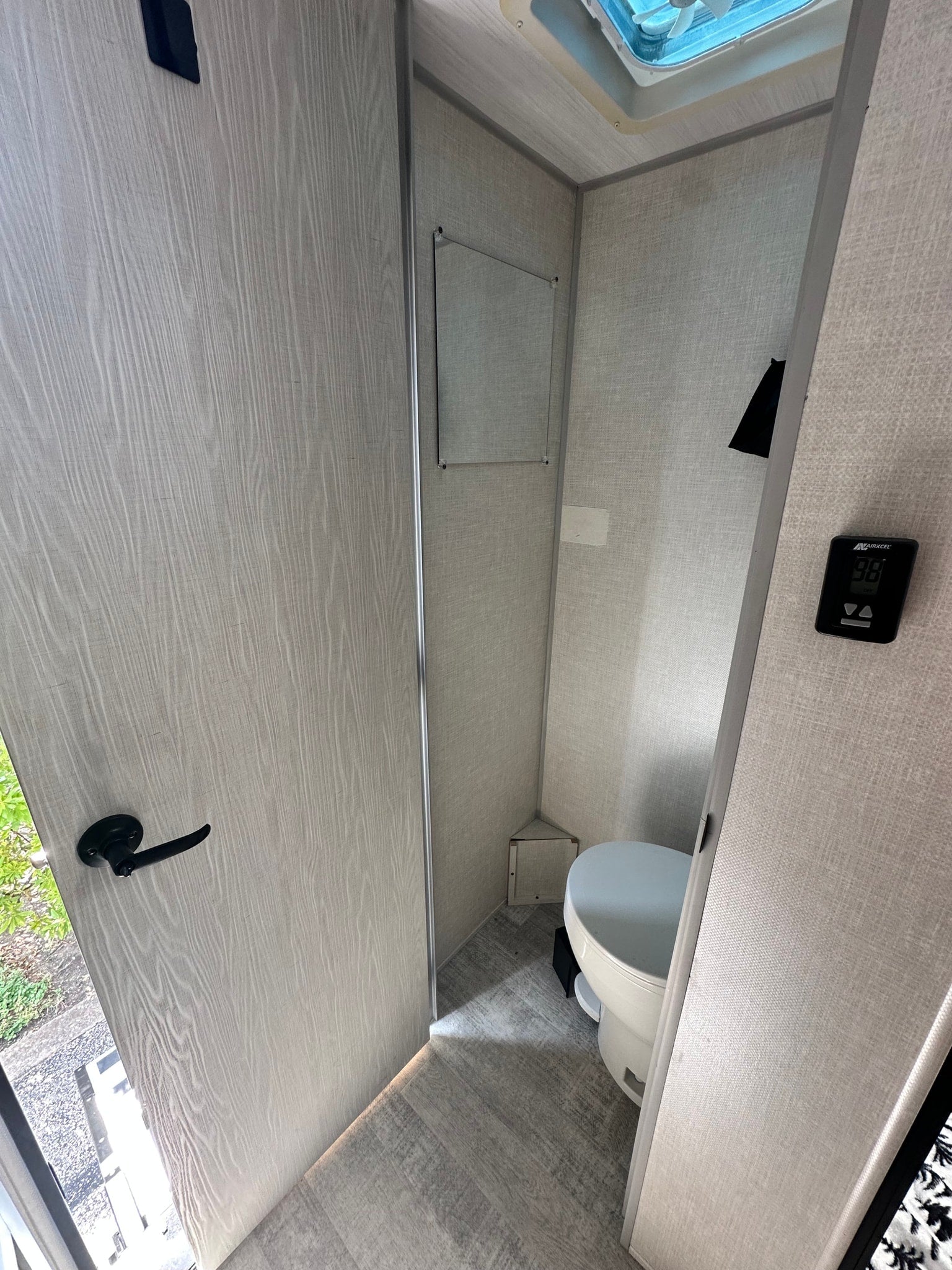 This compact RV rental bathroom features a white toilet on the right, a mirror, overhead vent, and digital climate control.
