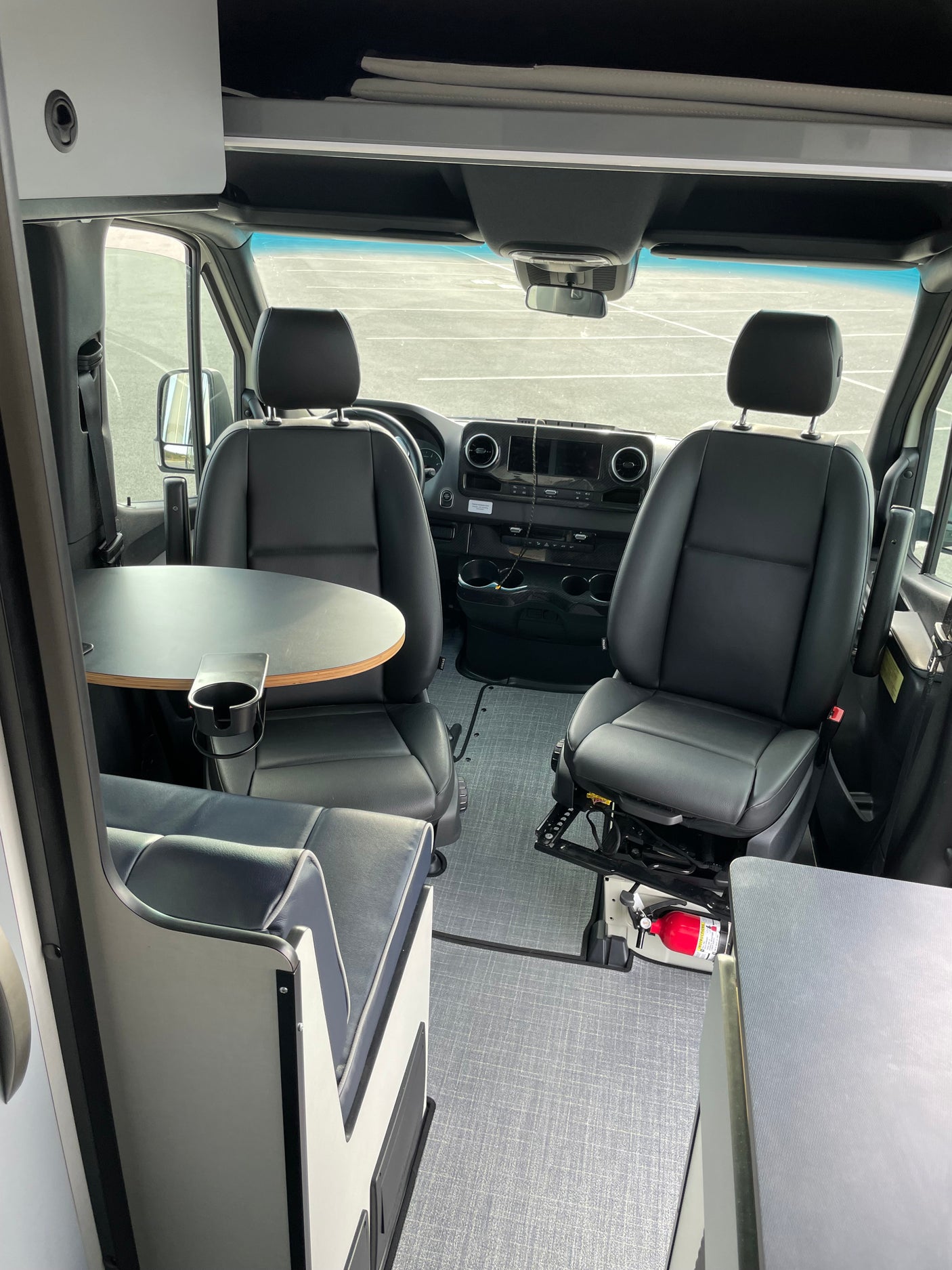 Spacious RV rental van interior with swiveling front seats, dinette table, and overhead storage. Fire extinguisher by passenger.