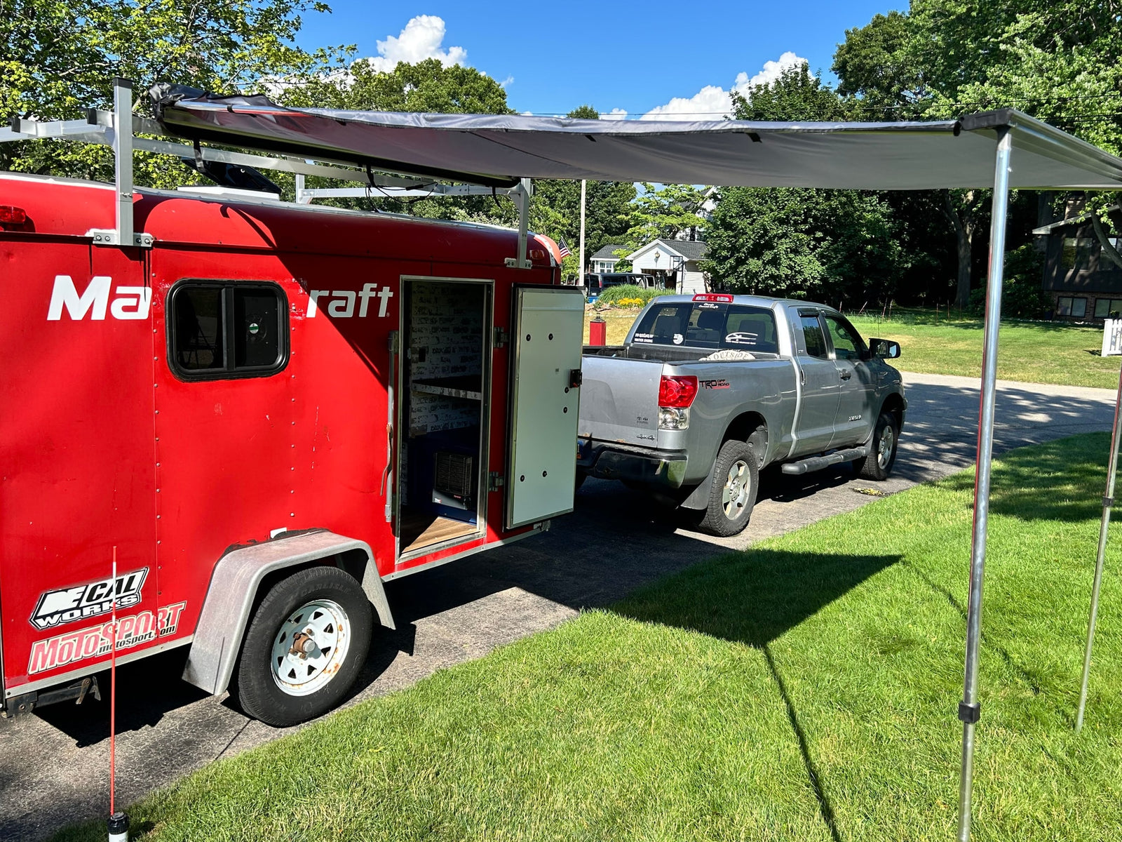 Motorsport trailer with open side, deployed awning, hitched to a silver pickup. Explore options for RV rental adventures.