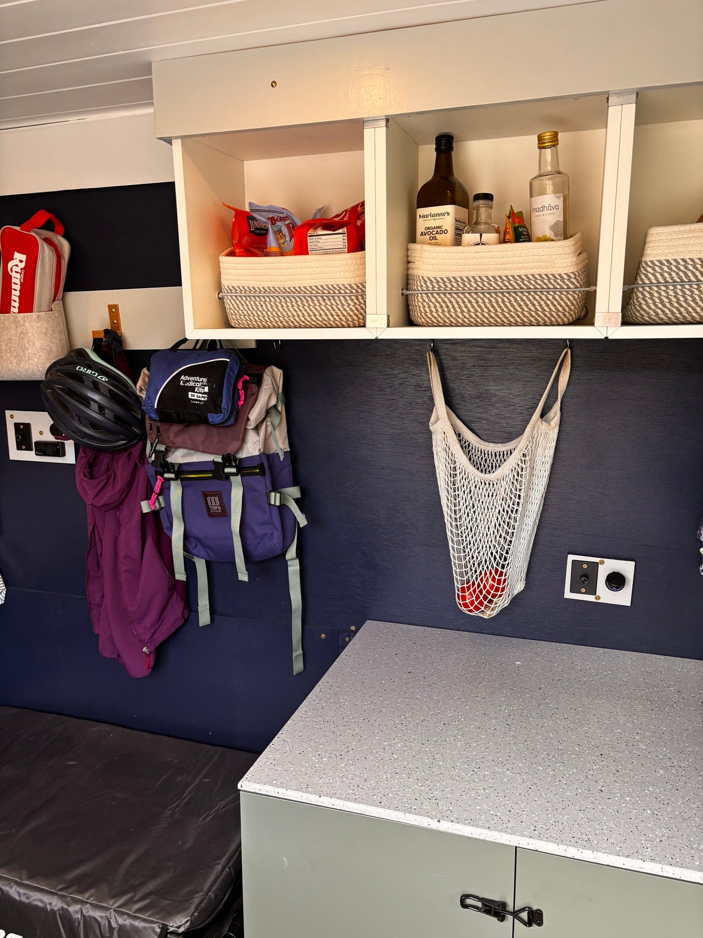 RV rental interior showing compact storage: overhead shelves with baskets, hanging gear, and kitchen essentials for travel.