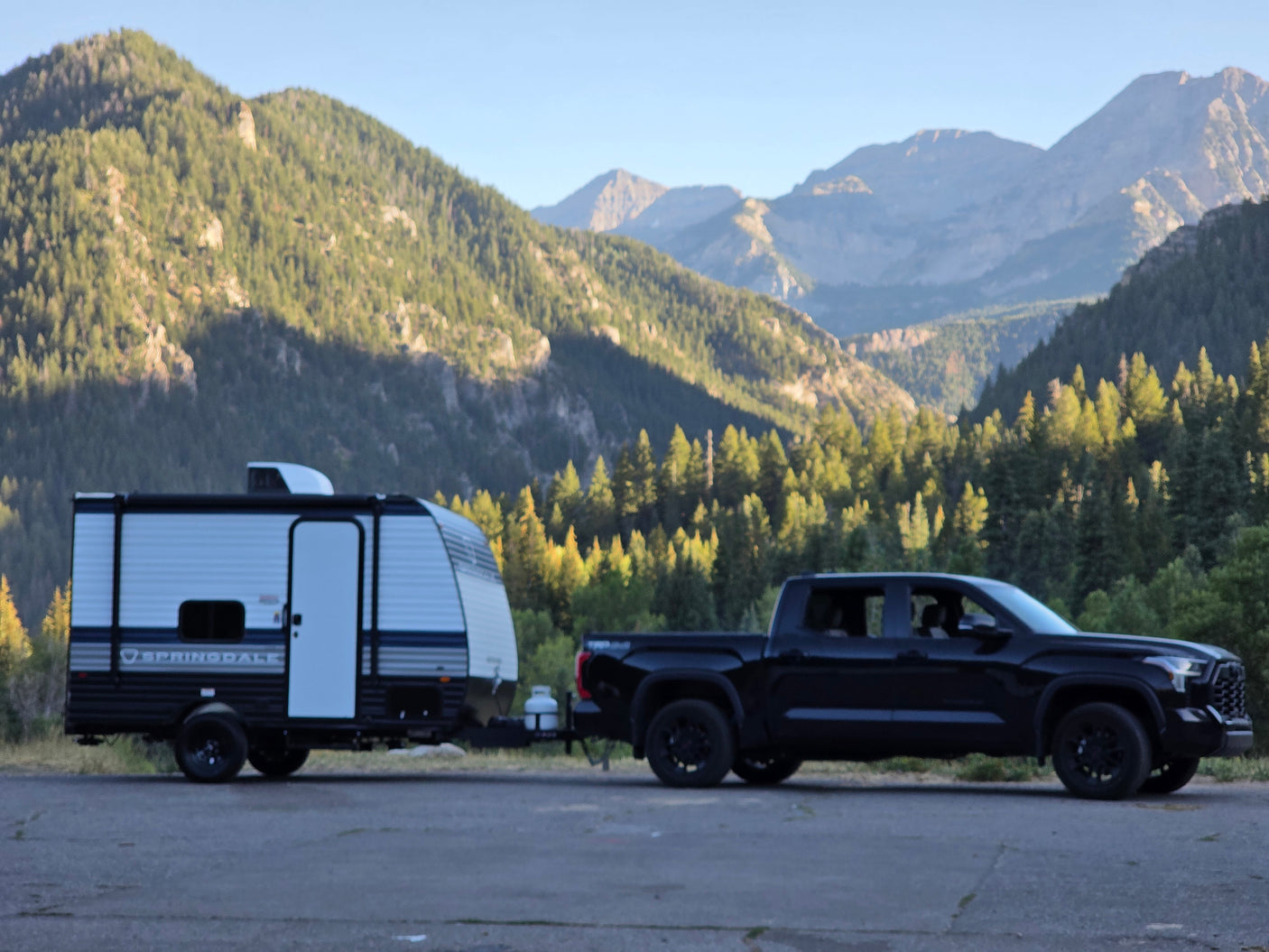 Scenic mountain travel with an RV rental: A black truck pulls a white camper, surrounded by majestic, forested peaks.
