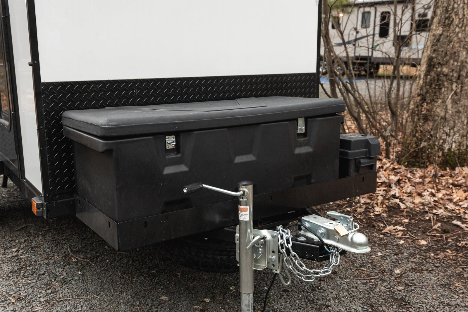 Front of an RV rental travel trailer showing its hitch, safety chains, jack, and a large black storage box.