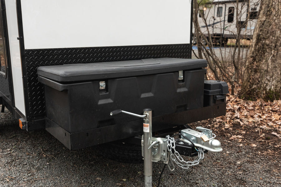 Front of an RV rental travel trailer showing its hitch, safety chains, jack, and a large black storage box.