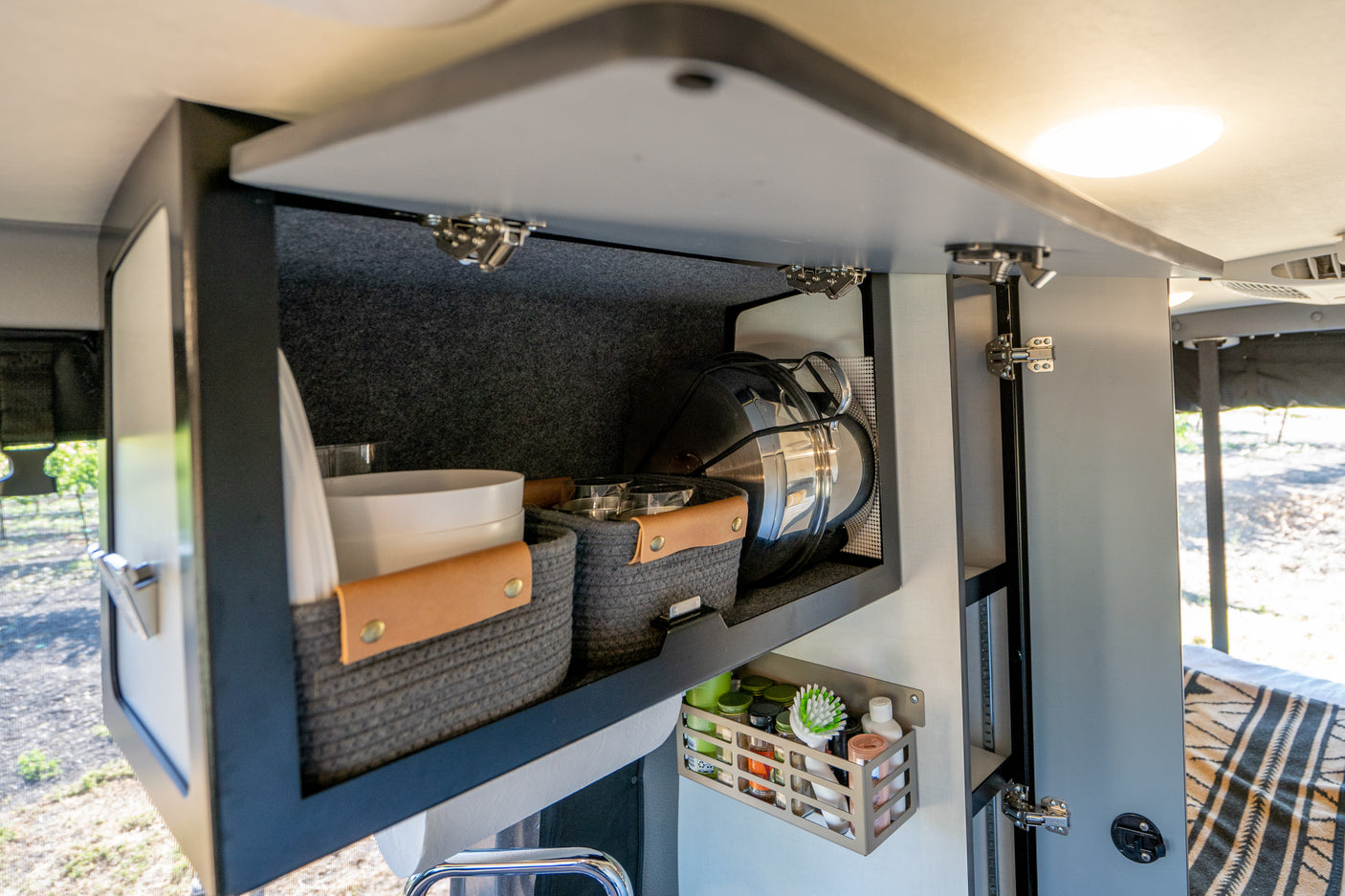 Well-organized RV rental kitchen cabinets with dishes, cookware, and spices, showcasing efficient travel storage solutions.