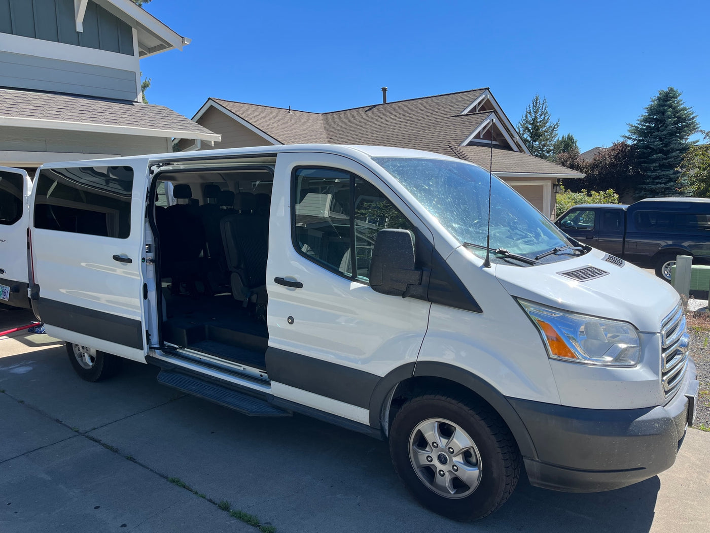 White Ford Transit passenger van, ideal for RV rental, parked with its side door open showing rows of seats. — photo 1