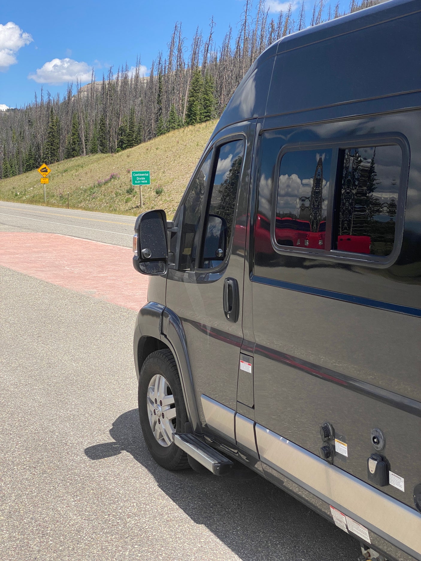 A dark grey RV rental at Continental Divide, 9858 ft. Located on a mountain road with many dead trees, ready for adventure.