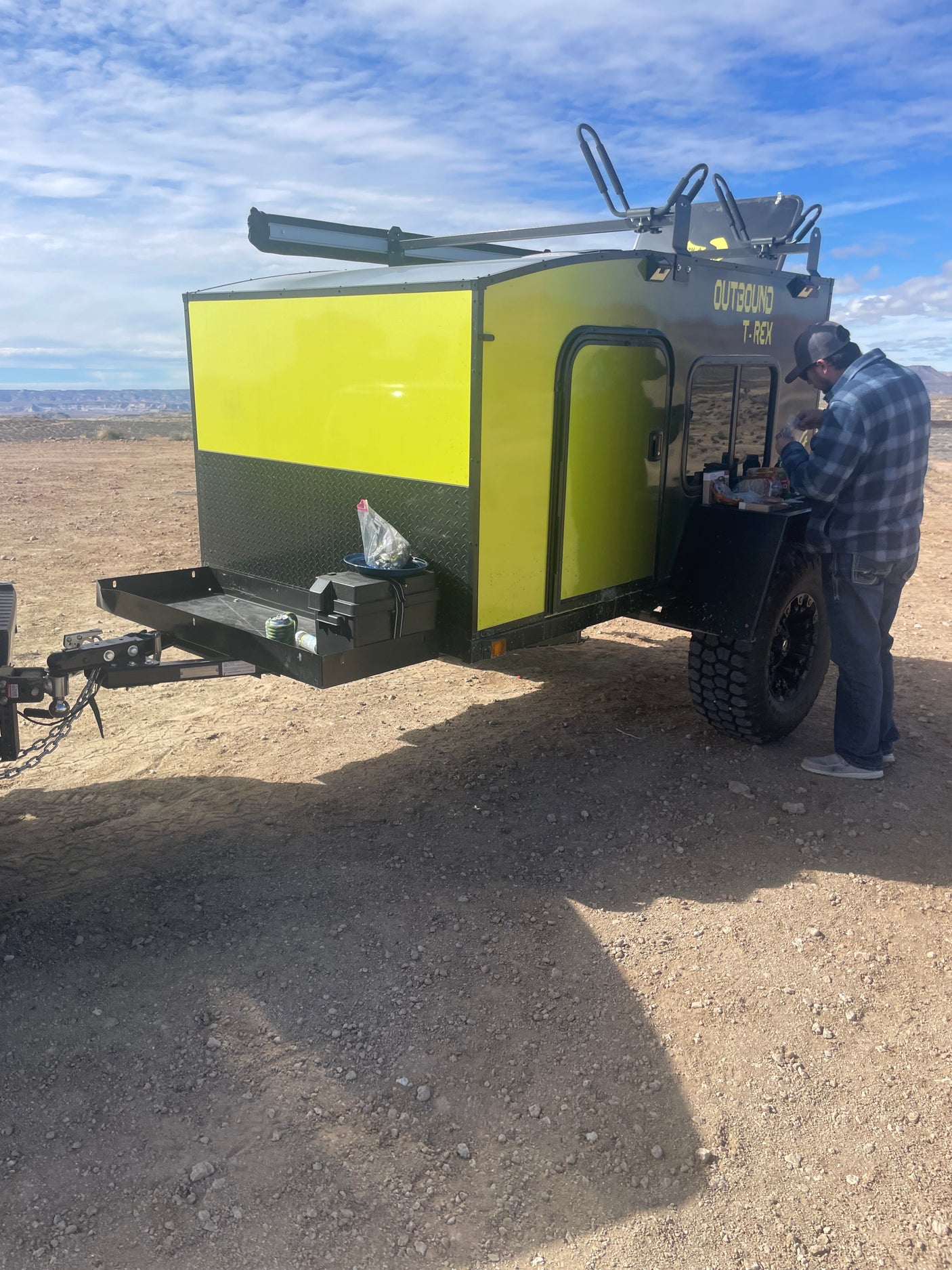 A man attends to a bright yellow Outbound T-Rex overland trailer. This RV rental is perfect for desert camping adventures.
