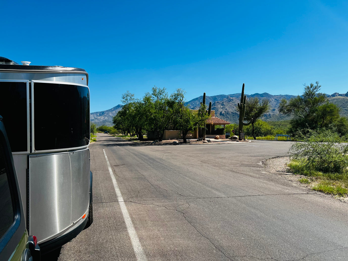 Scenic RV rental journey: A silver travel trailer parked at a desert park entrance with saguaro cacti and mountains.