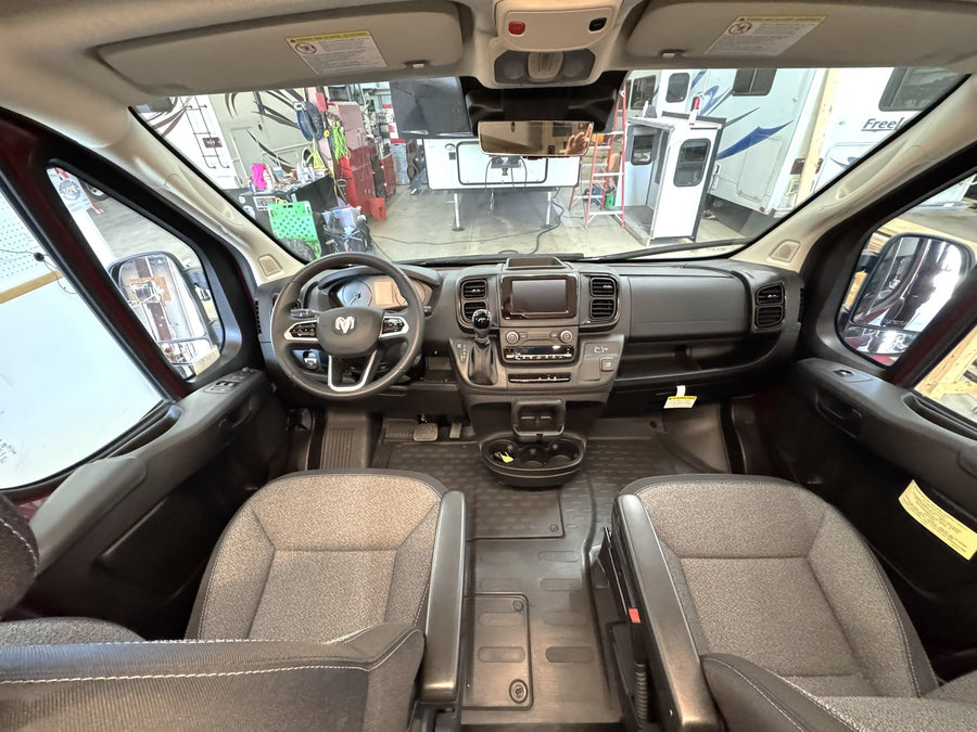 Inside a modern camper van (RV rental) cockpit. View of dashboard, steering wheel, and front seats, ready for adventure.