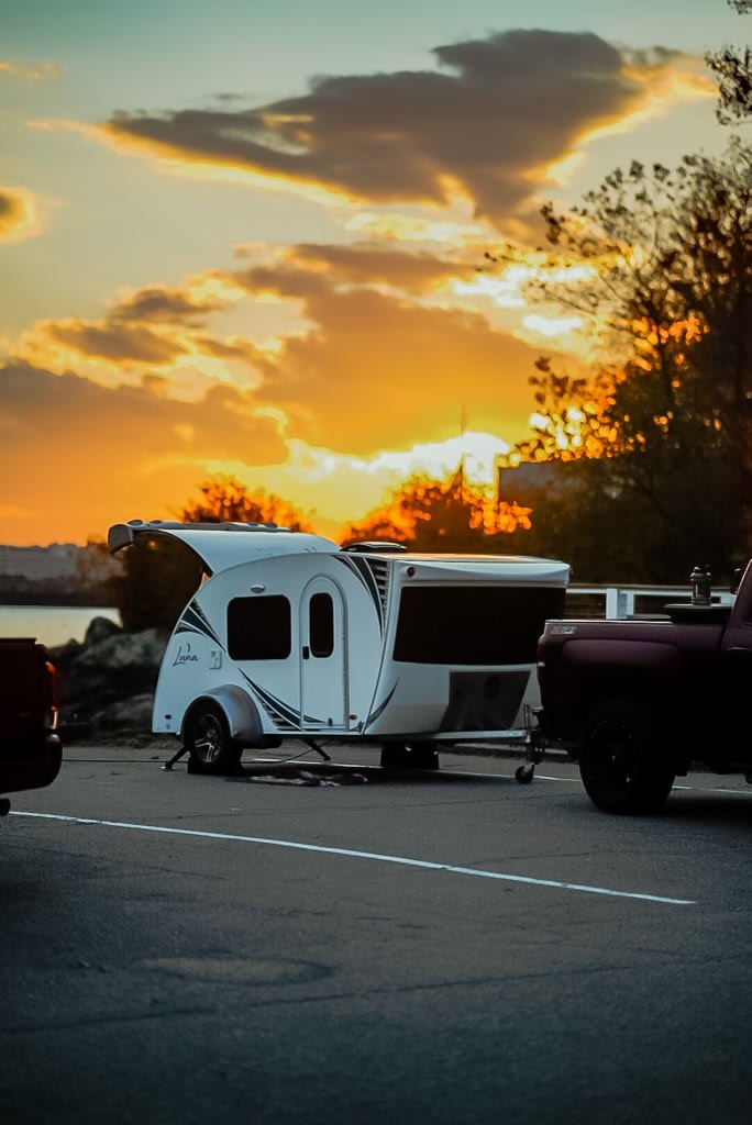 A white teardrop camper hitched to a red truck