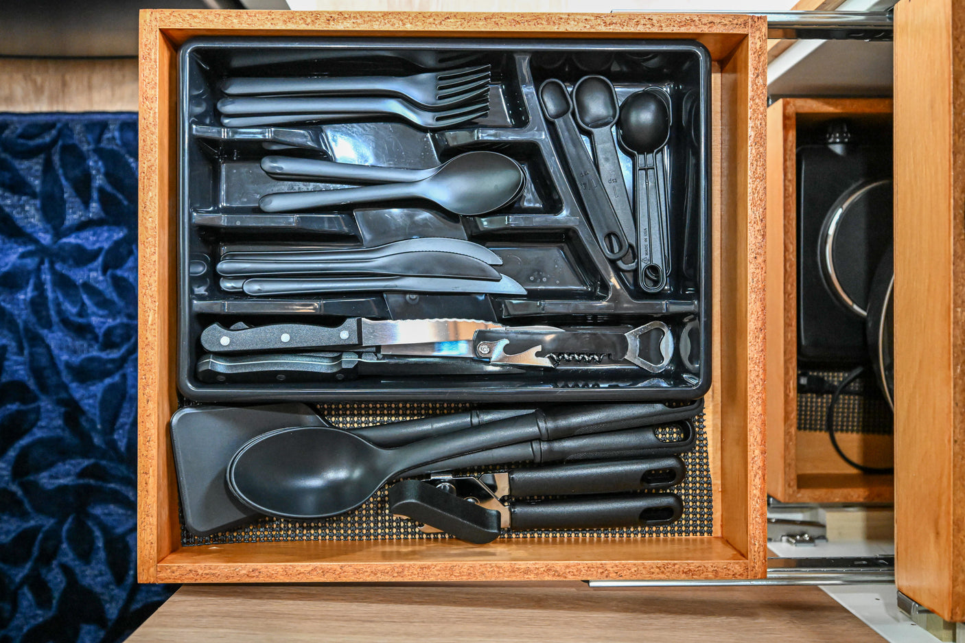 Neatly organized kitchen utensils drawer with cutlery & cooking tools, ideal for an rv rental. Visually, black tray in wooden drawer.
