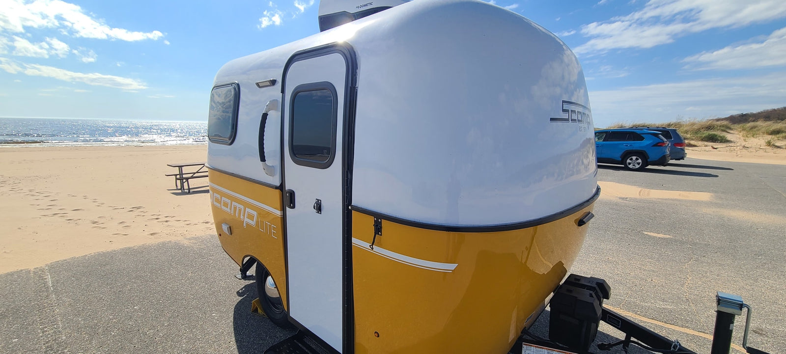 This yellow & white Scamp rv rental is perfectly parked beachside, ready for coastal adventures by the sparkling ocean.