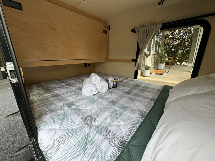 and an open hatch revealing an outdoor patio. Ready for adventures!|Cozy RV rental interior: A compact bed with plaid bedding