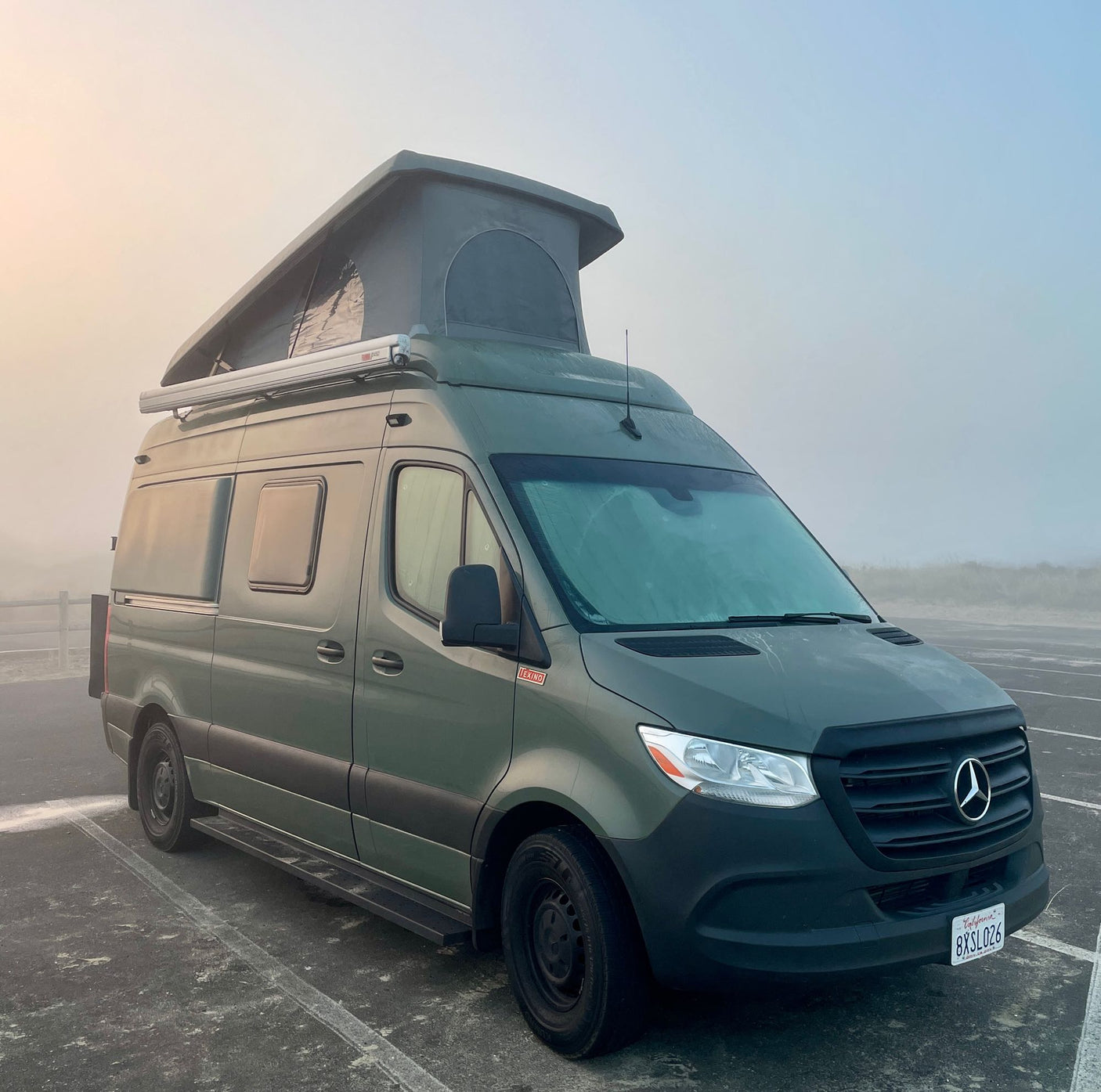Green Mercedes-Benz Sprinter camper van, an ideal RV rental, parked in a foggy outdoor lot.