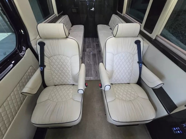 featuring tinted windows & an awning. Perfect for luxury road trips.|Luxurious RV rental interior: two cream quilted captain's chairs with side benches. Plush seating for road trips.|Plush RV rental interior: cream seats
