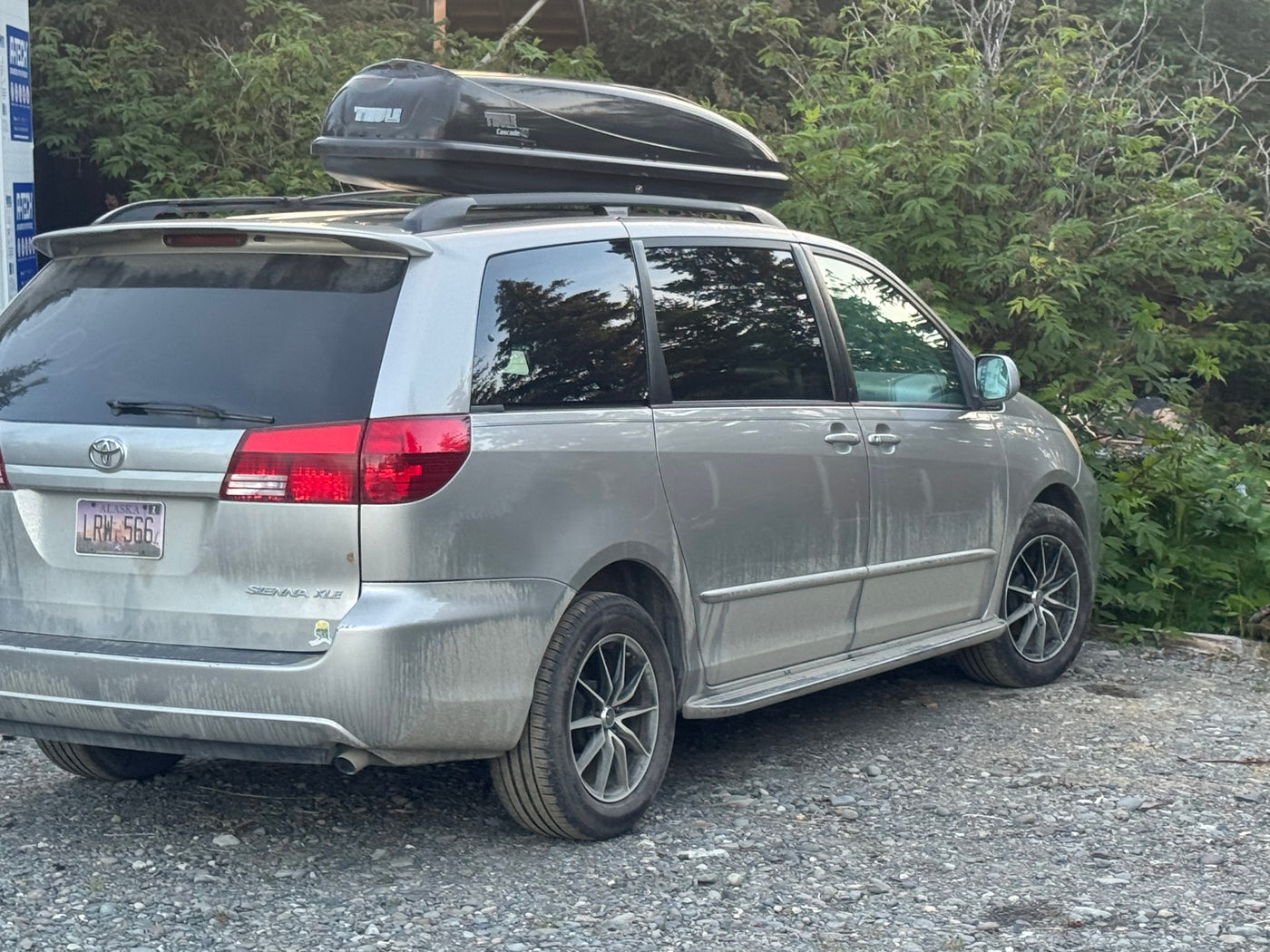 parked on gravel. Green foliage and trees visible. Could be near an rv rental office.|This minivan features a comfortable red plaid bed — photo 11