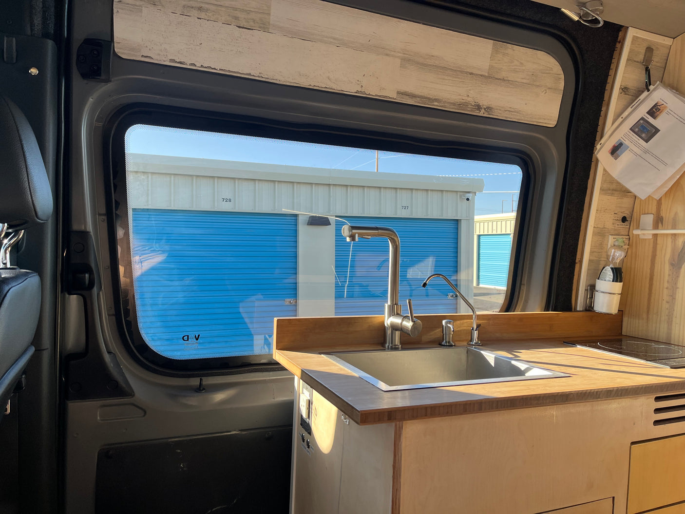 An rv rental's interior reveals a neat kitchen with a sink, faucet, and wood counter, overlooking blue storage units.