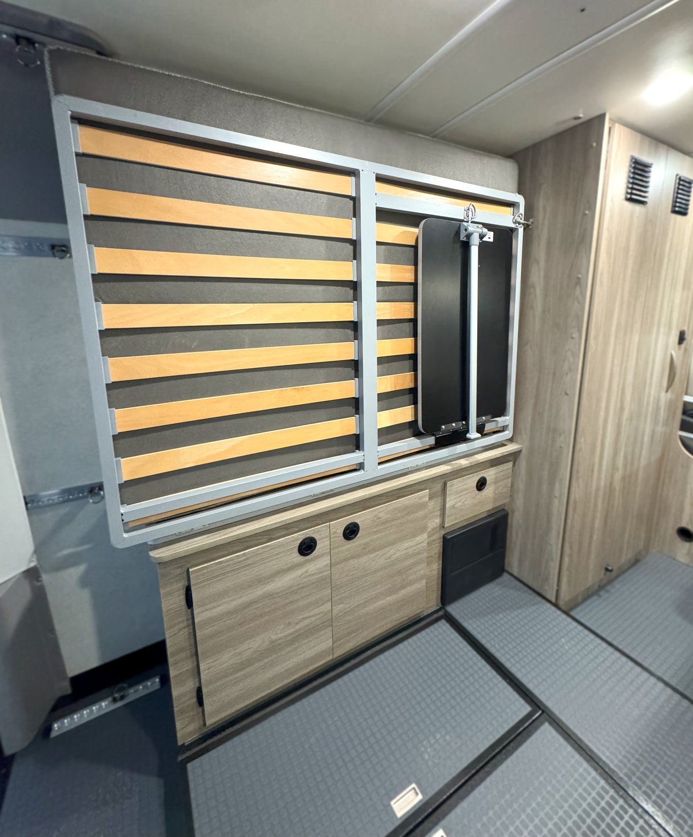 This RV rental's camper interior features a folded slatted bed, built-in storage cabinets, and durable flooring.