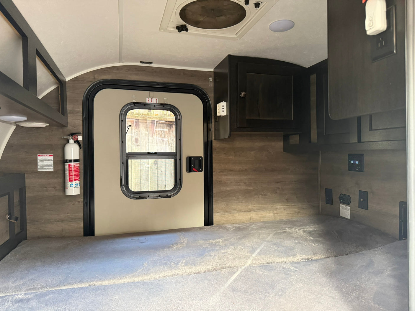 Inside a cozy rv rental: a bed, door, fire extinguisher, and overhead cabinets, ready for your next travel adventure.