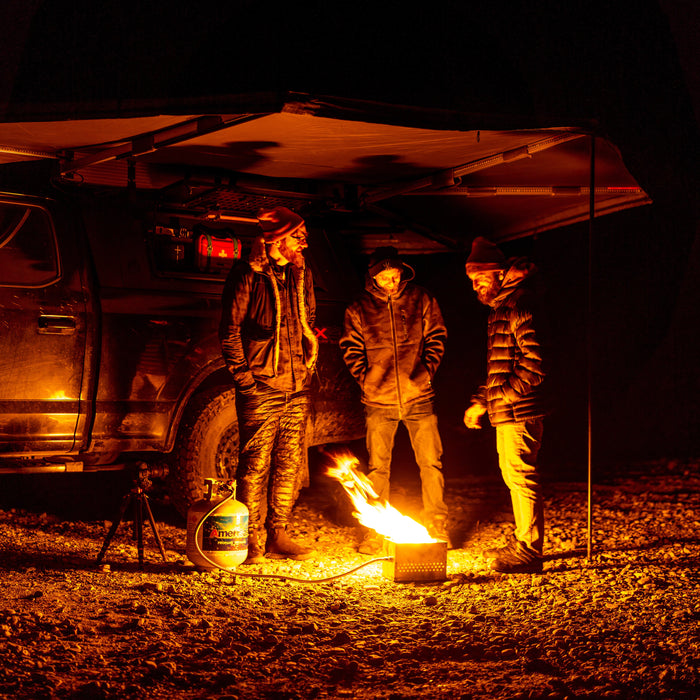 Night camping under an RV rental awning. Three men gathered around a cozy fire pit, enjoying the outdoors.