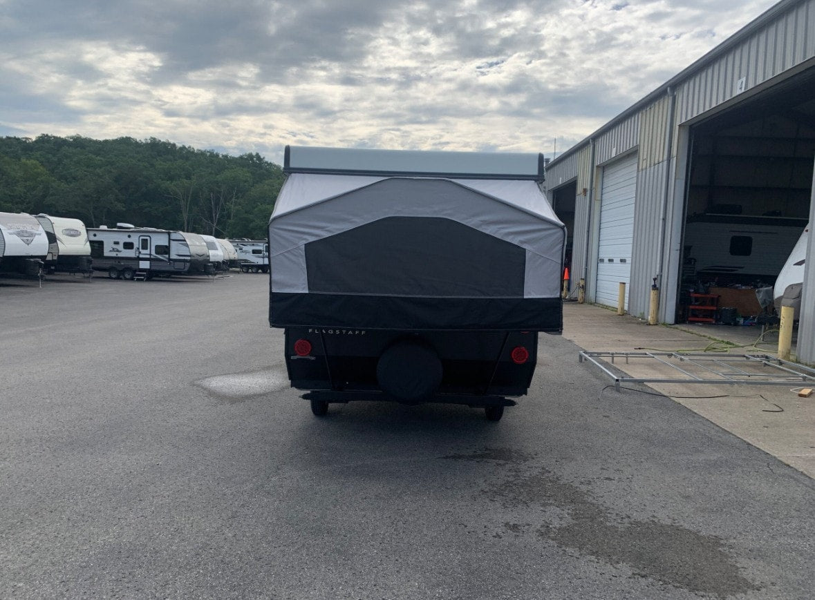 This Flagstaff pop-up camper, a great RV rental option, is shown from the rear in a lot with other travel trailers and a service building.