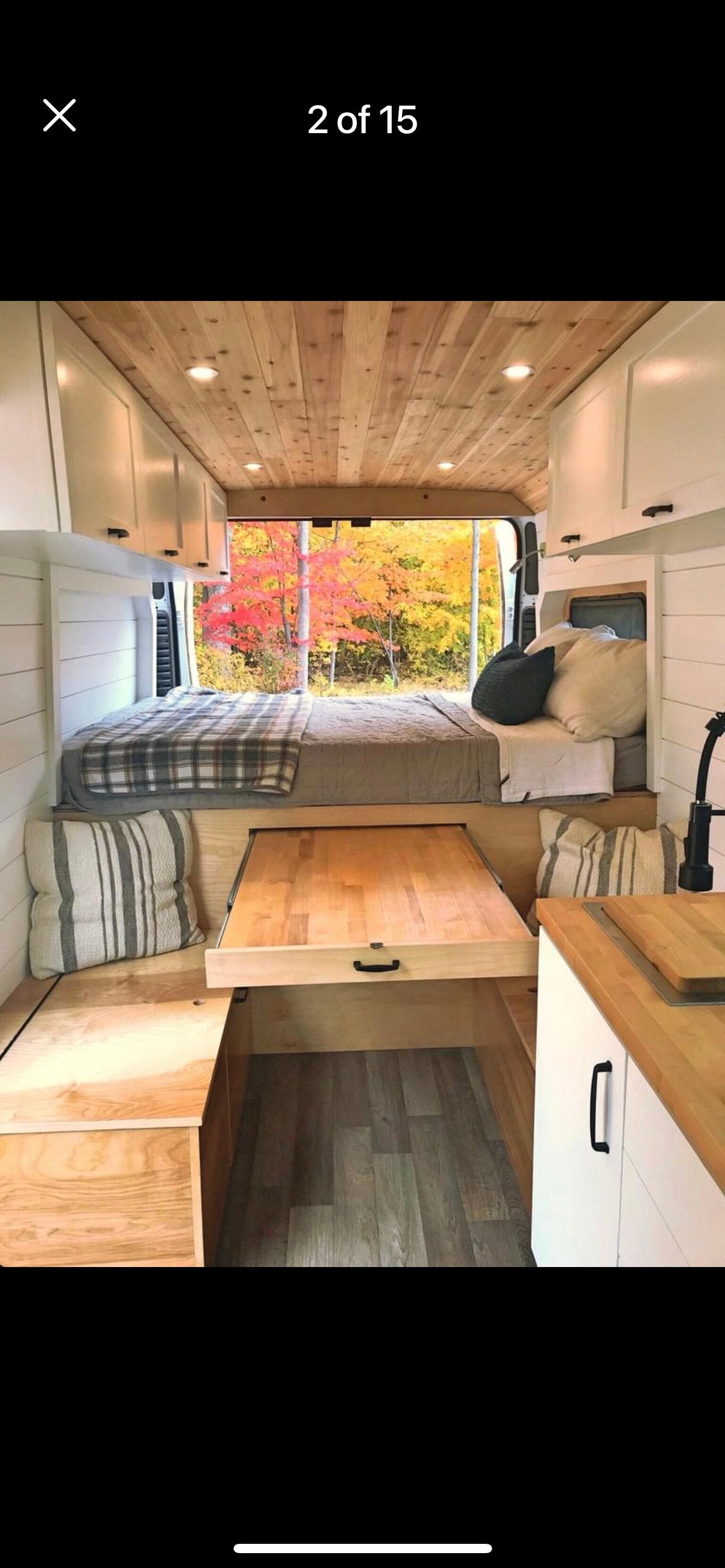 Spacious RV rental interior featuring a cozy bed, pull-out table, kitchen, wood ceiling, and stunning autumn views.