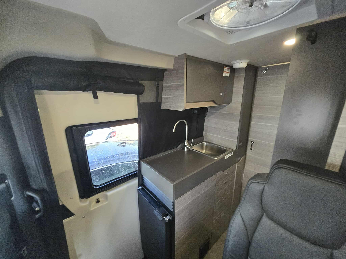 RV rental: Compact camper van interior with a kitchen counter, sink, overhead cabinet, small fridge, and front seat.
