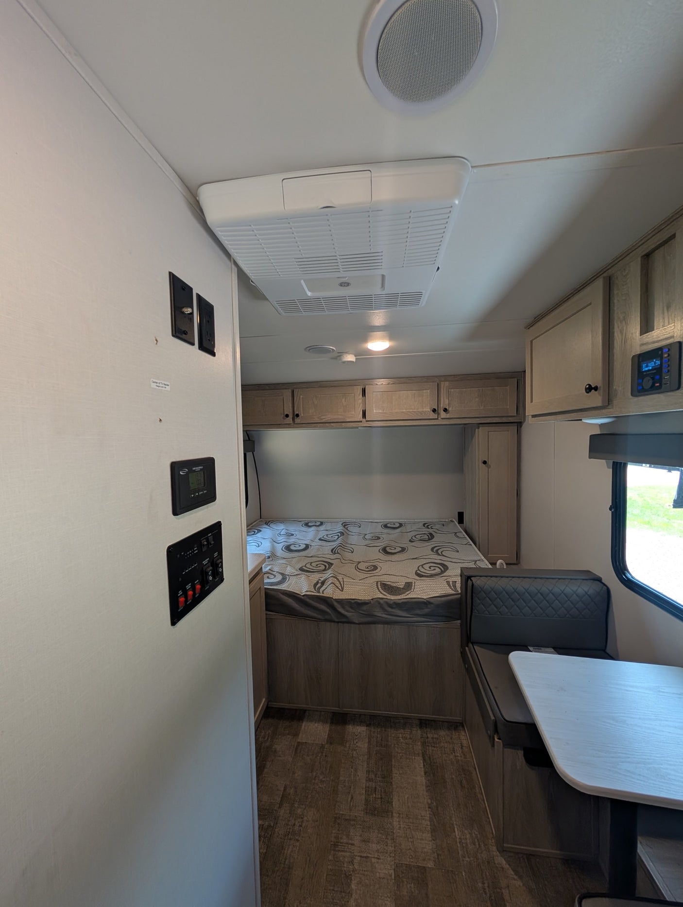 Inside this modern rv rental: a compact bedroom with overhead cabinets, a dinette, and essential controls for your trip.