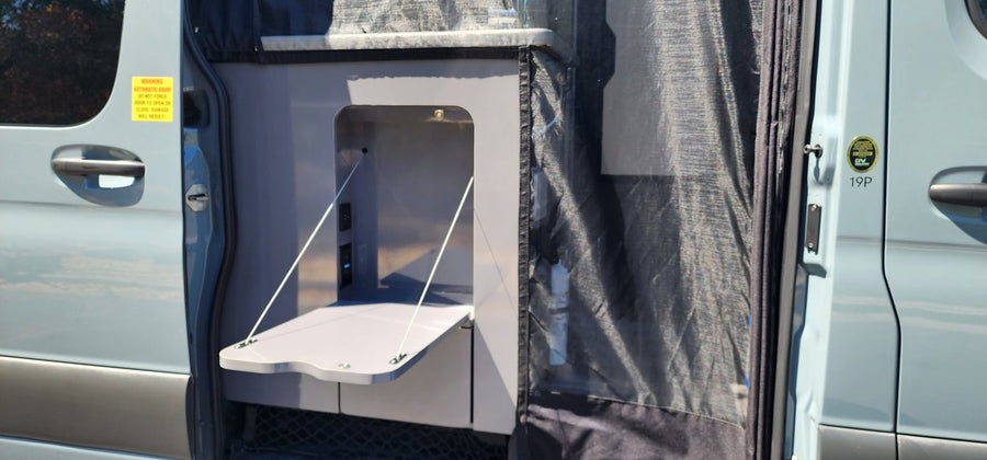 Interior of an RV rental van, featuring an open side door with a fold-down table and power outlets.