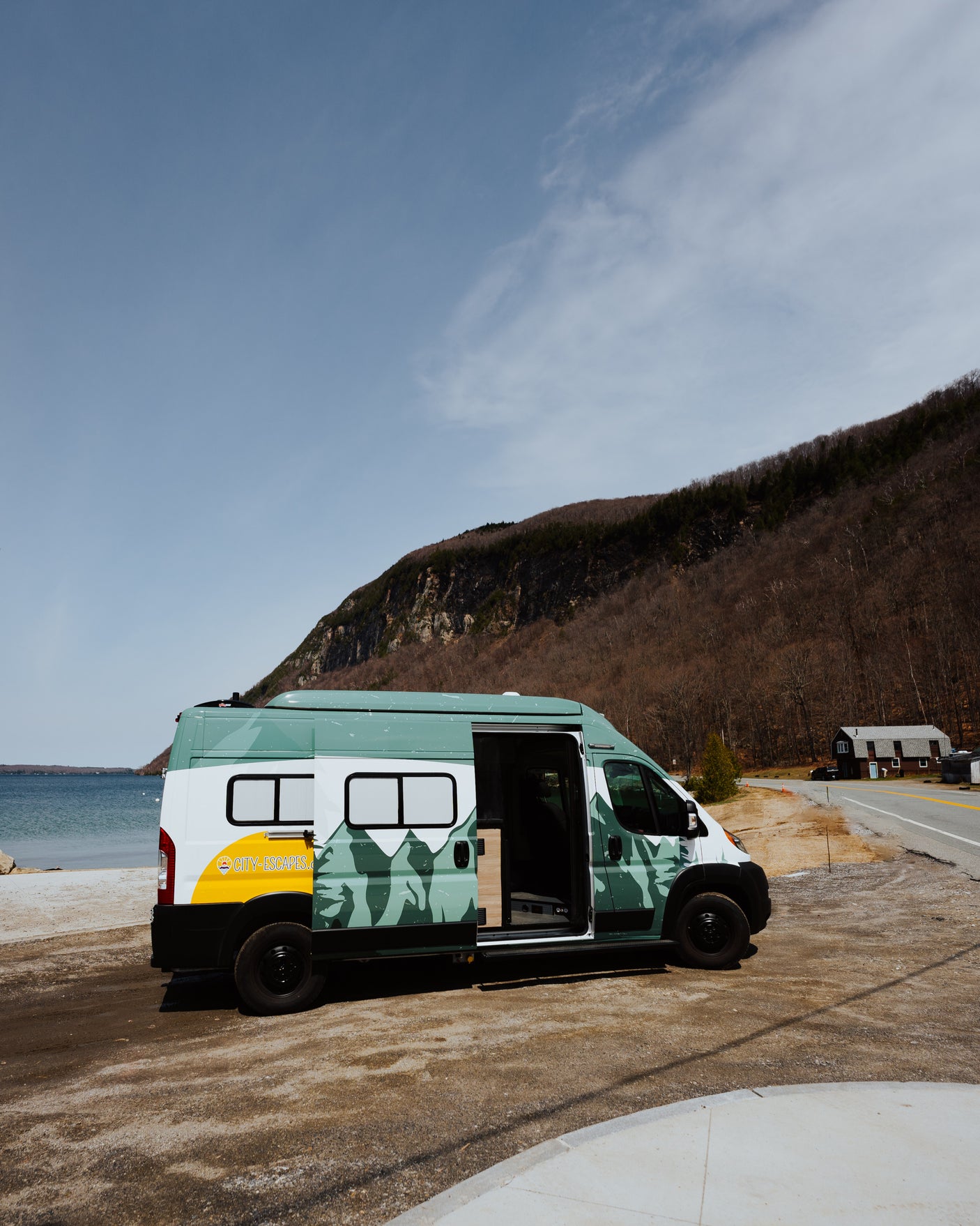 A custom teal & white RV rental van is parked lakeside, with a mountain backdrop. Ideal for scenic adventures.
