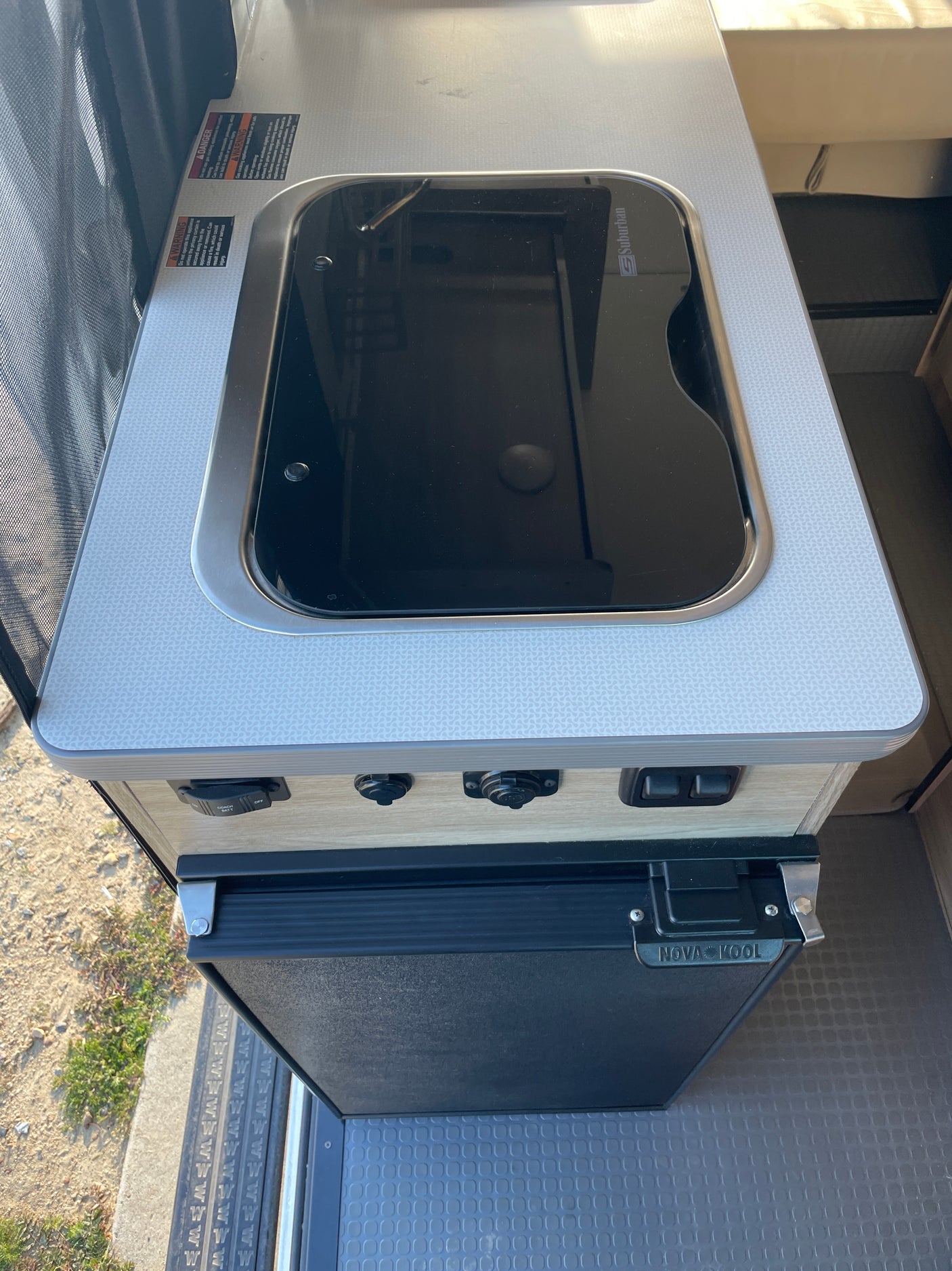 Explore this rv rental's compact kitchenette, featuring a Suburban stovetop/sink, Nova Kool fridge, and essential controls.