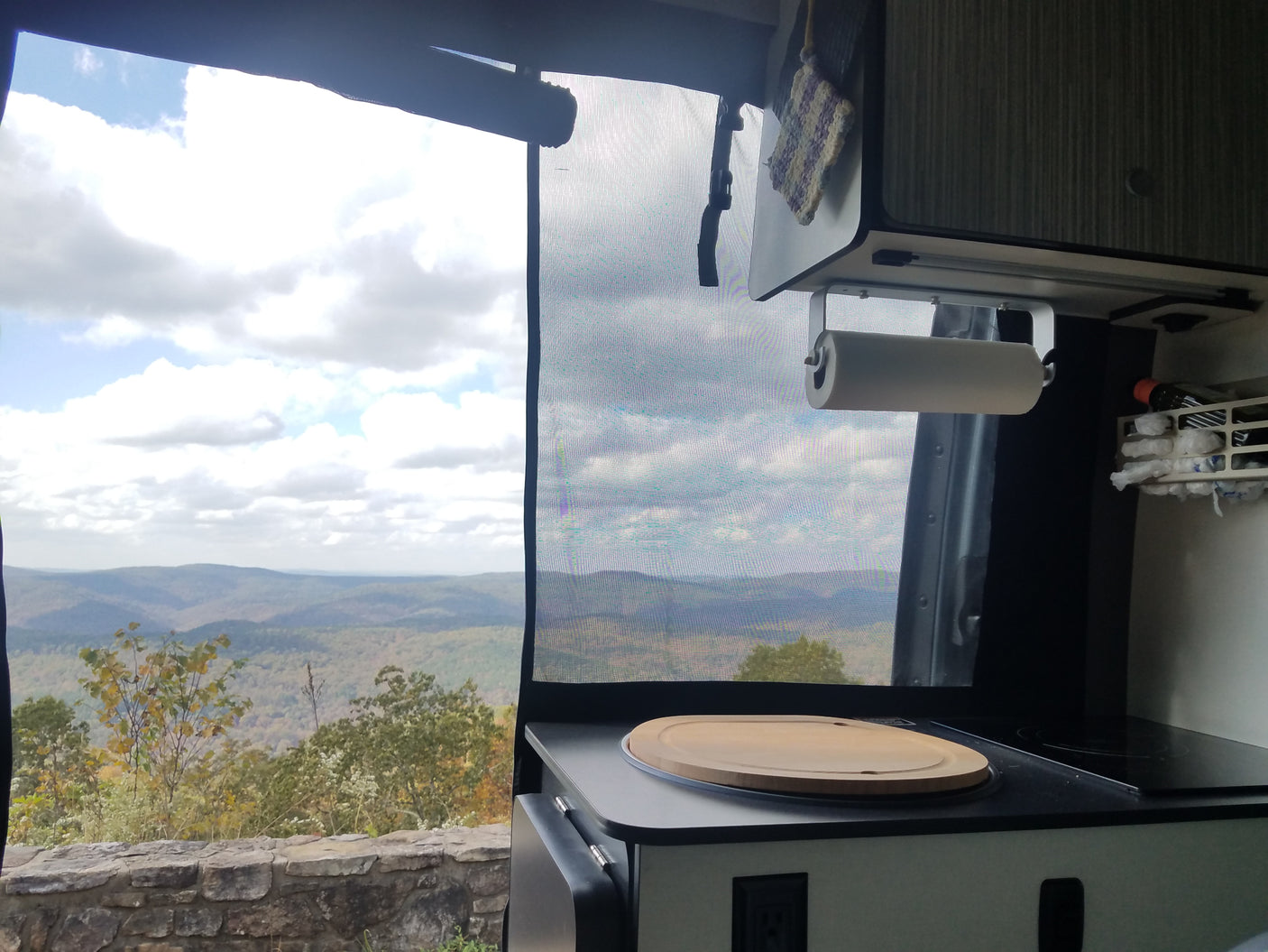 Stunning mountain view from an RV rental, showcasing the camper van's functional kitchen counter, cooktop, and paper towel holder.