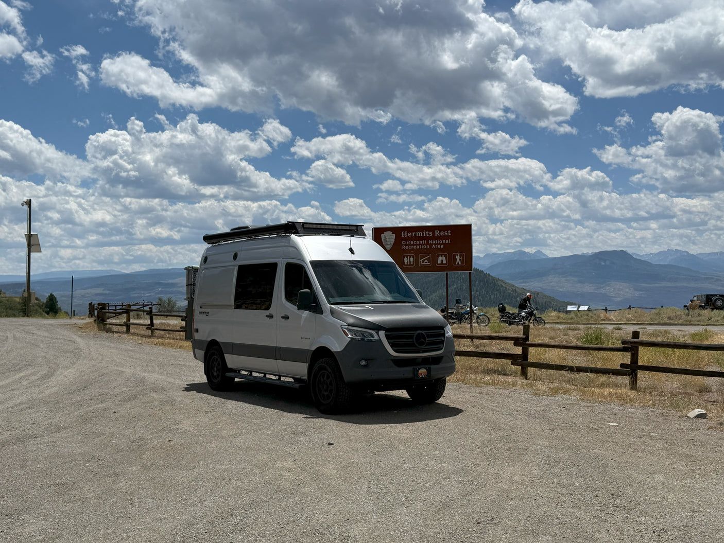White RV rental (Sprinter van) at Hermits Rest, Curecanti National Recreation Area, offering scenic mountain views under cloudy skies.