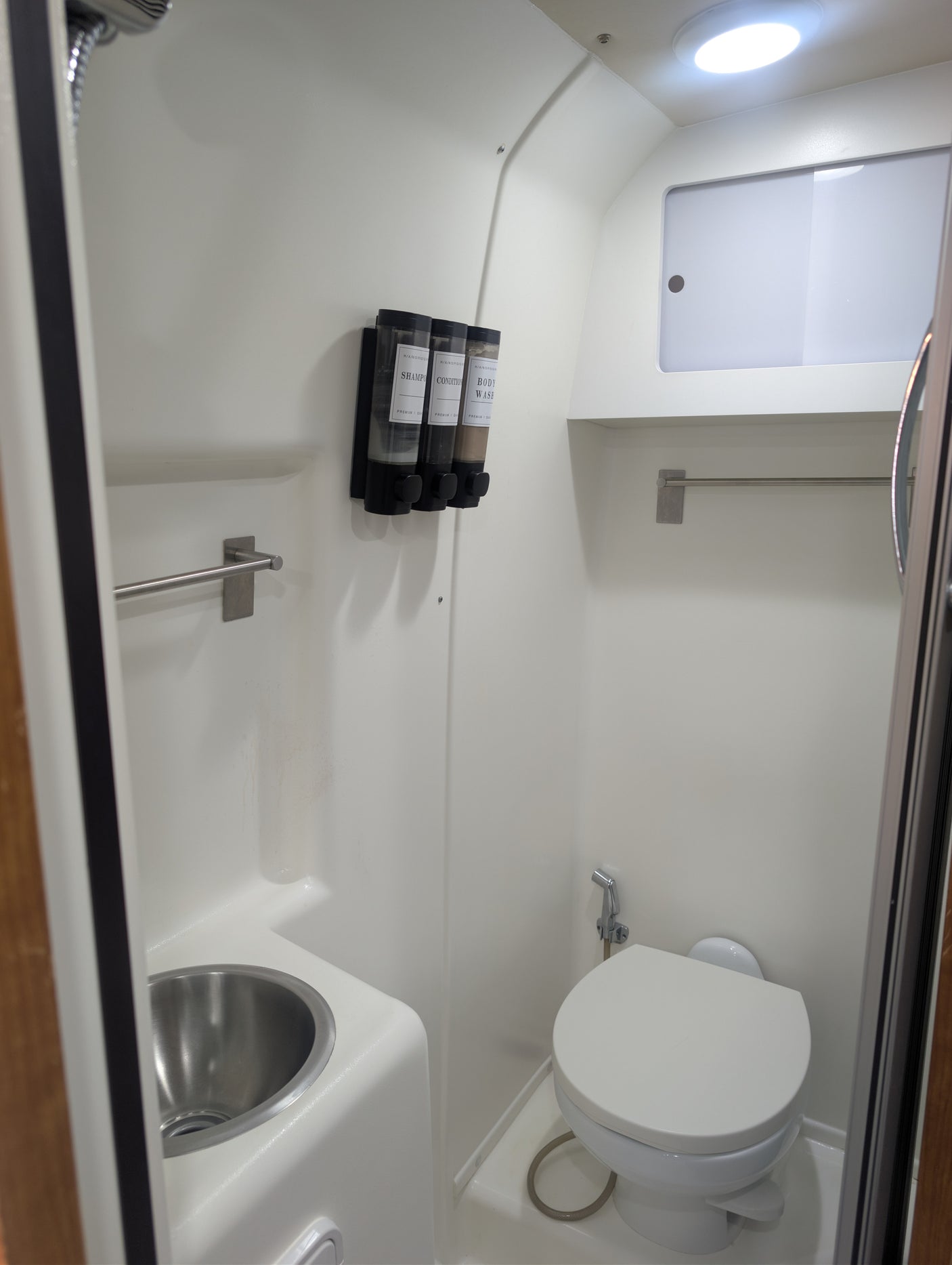This clean, compact bathroom in an RV rental includes a toilet, small sink, shower, and wall-mounted shampoo/soap dispensers.