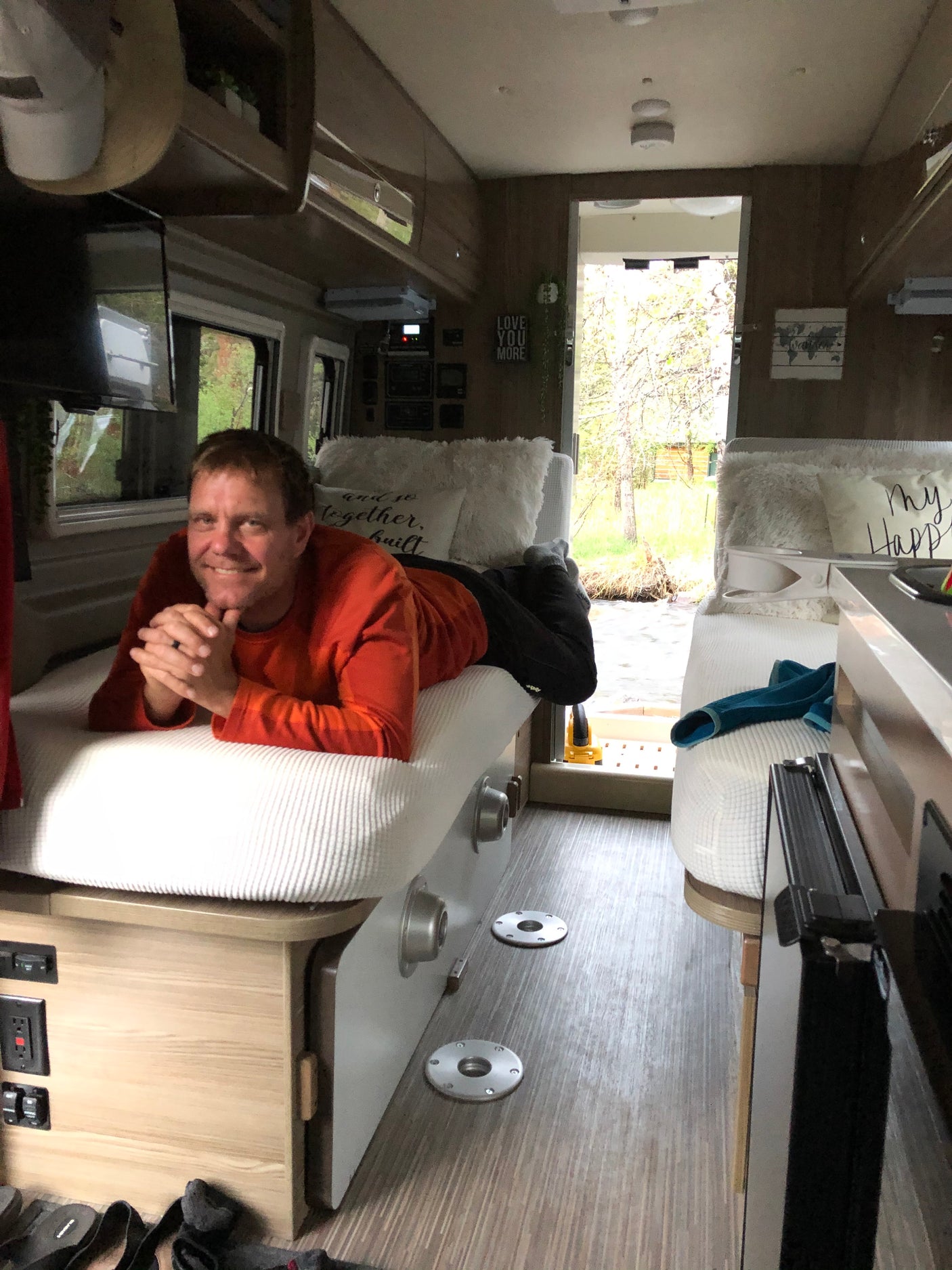 Man smiles from a comfortable bed in an RV rental, overlooking a scenic outdoor view. Ideal for travel and relaxation.