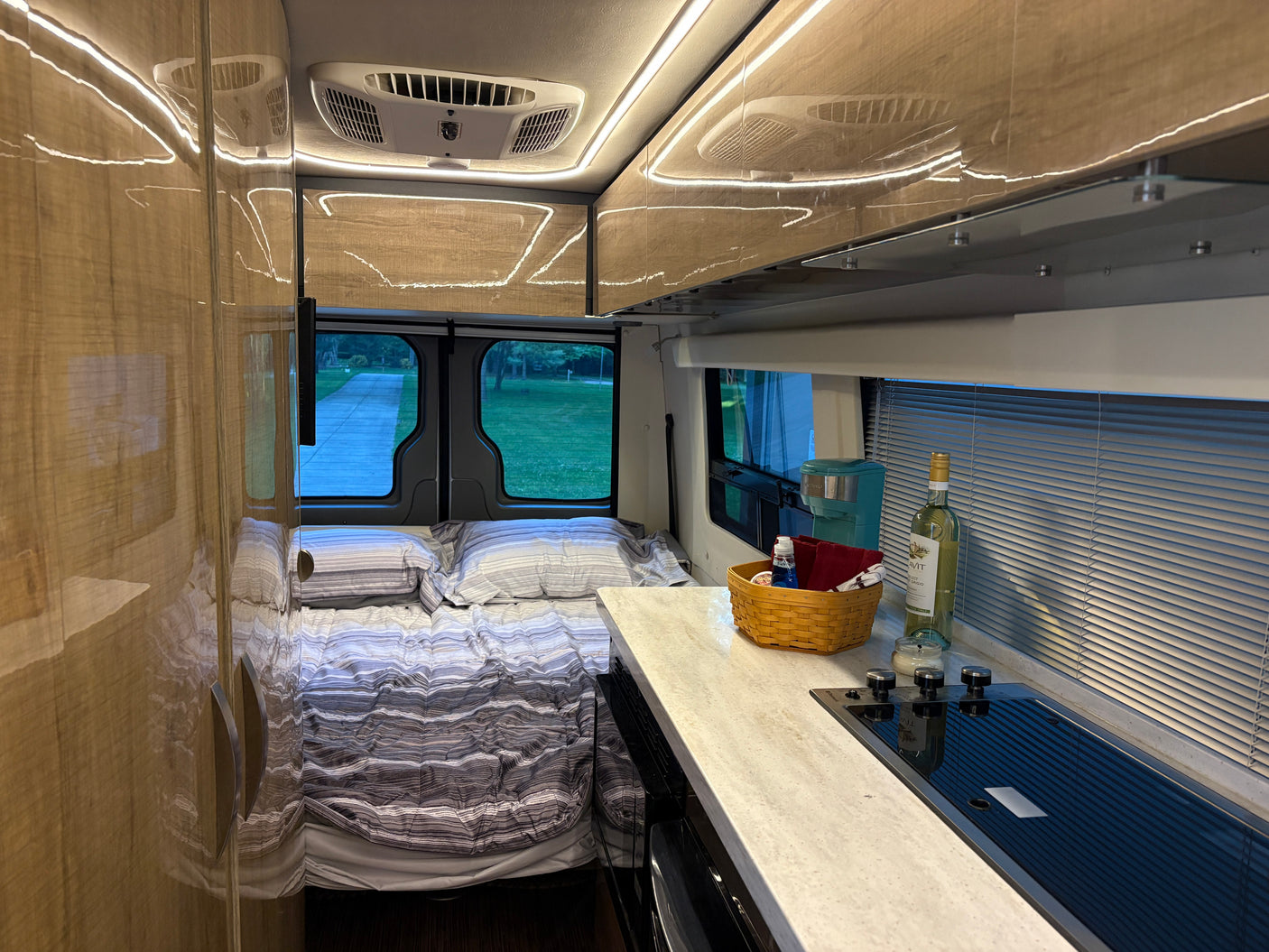Modern rv rental interior: a comfy bed, sleek kitchen counter with stove, and warm overhead lighting. Ready for travel!