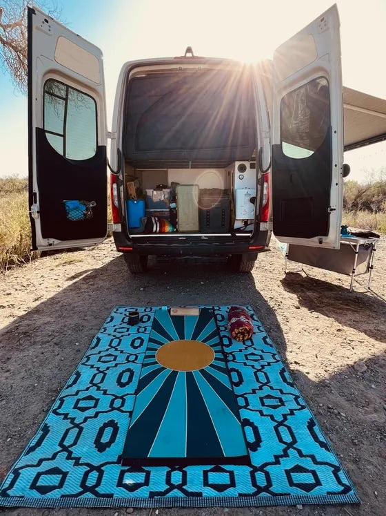RV rental adventure: Van's open doors reveal organized camping gear & a comfy mat for outdoor living.