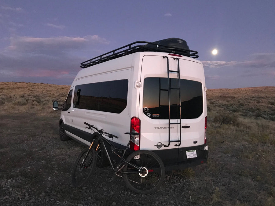Adventure-ready RV rental: white camper van with bike, roof rack, under a full moon.