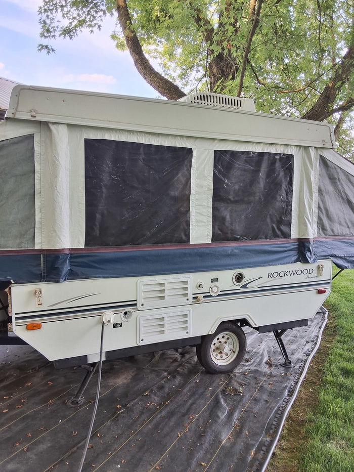 Explore with this Rockwood Premier pop-up RV rental. A white camper with canvas sides set up outdoors on a tarp.