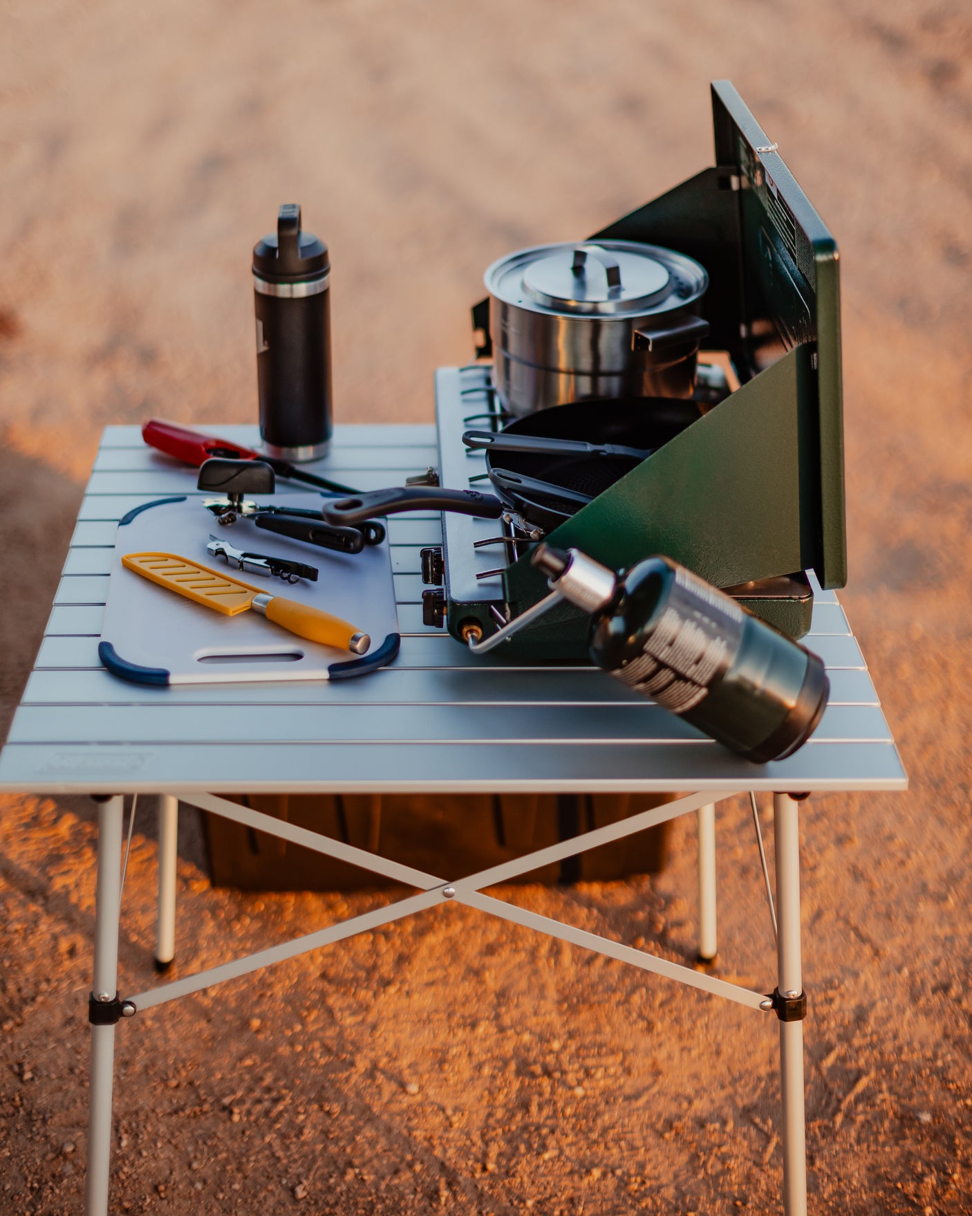 RV rental camp kitchen: Portable table with a green camping stove, pot, pan, cutting board, and diverse tools for outdoor cooking.