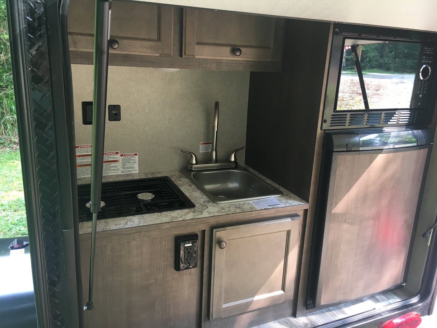 Compact RV rental kitchen features Dometic stovetop, sink, microwave, and refrigerator, ideal for travel.