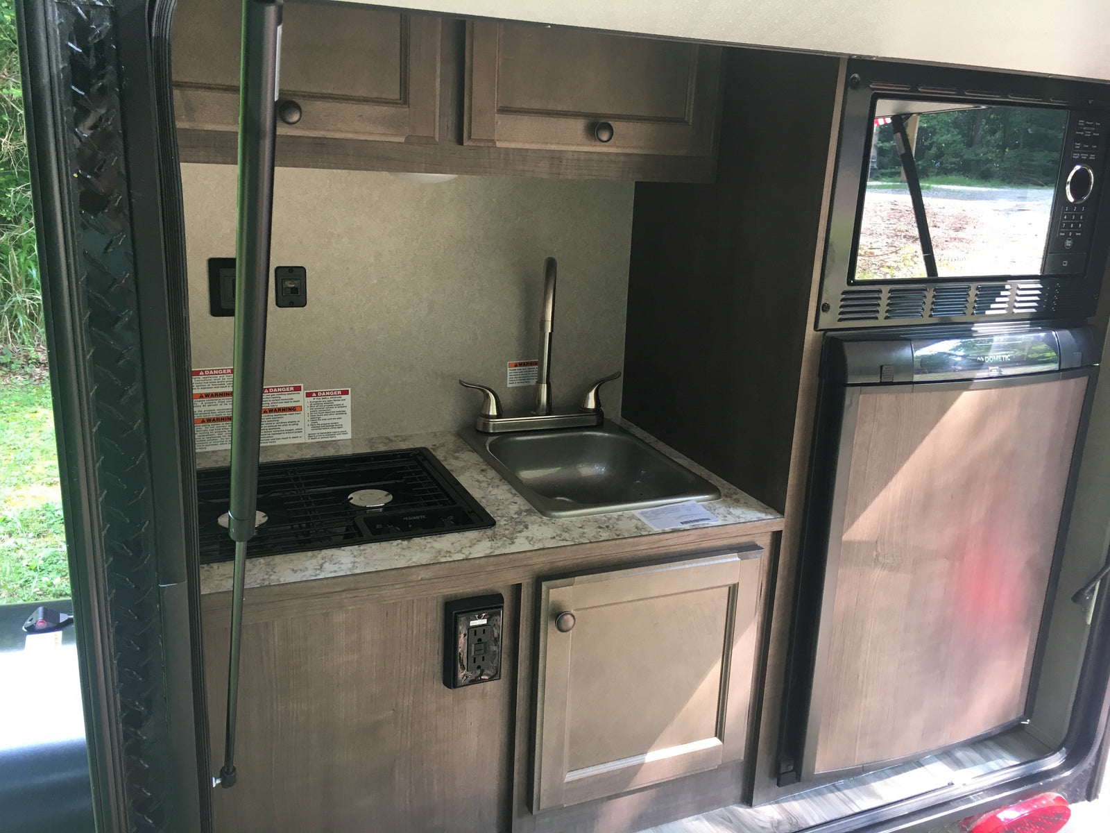 Compact RV rental kitchen features Dometic stovetop, sink, microwave, and refrigerator, ideal for travel.