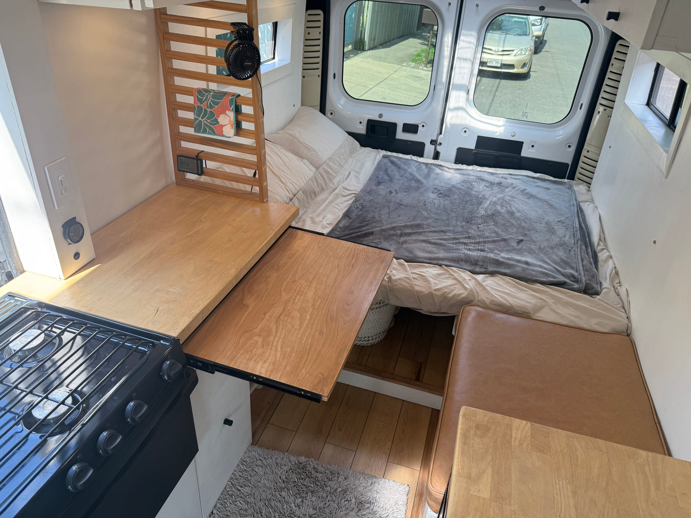 Inside an RV rental van, a full bed, gas stove with extending countertop, and seating create a compact living space.
