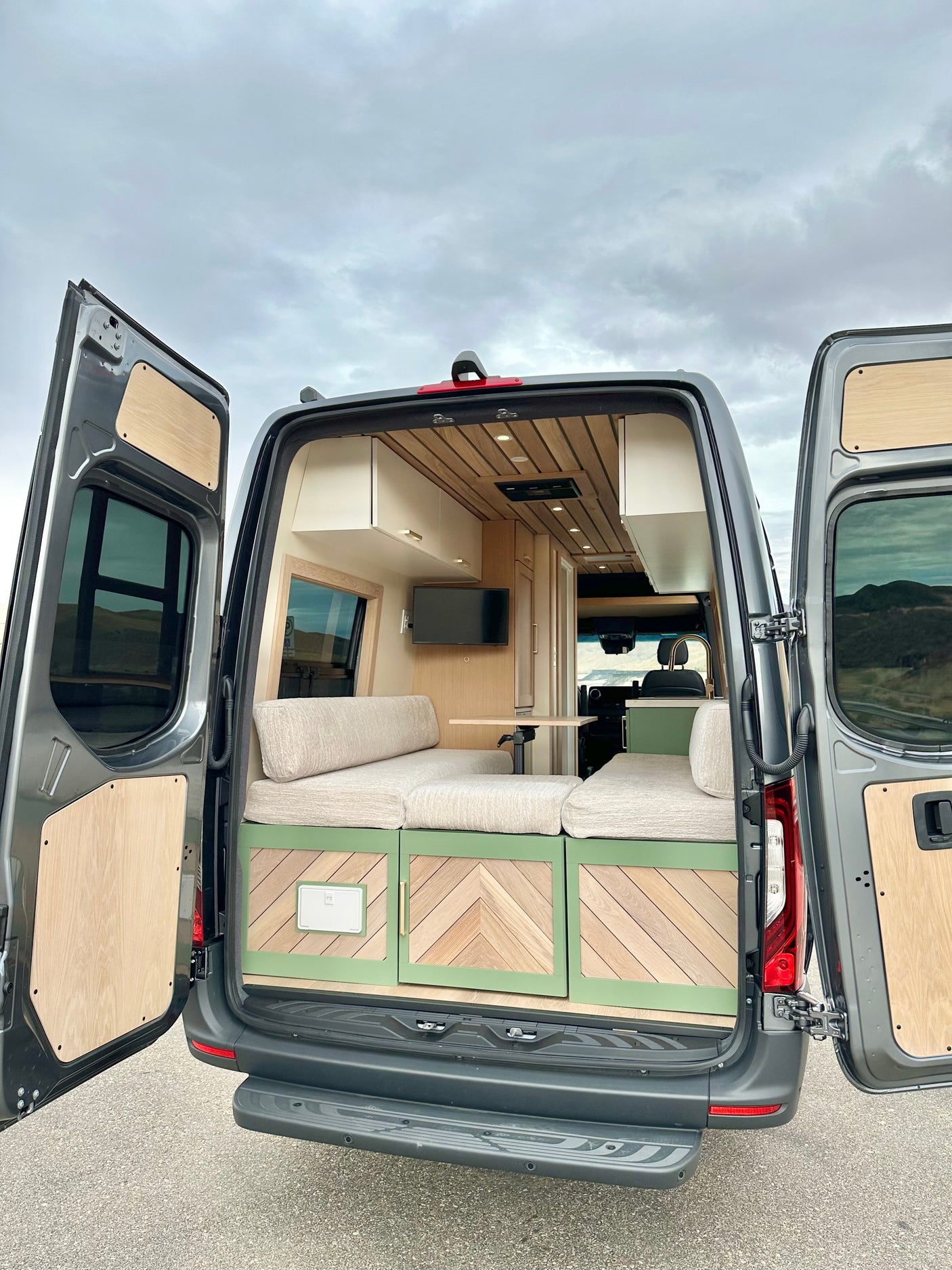 RV rental: Step into this custom grey camper van. Its chic interior features light wood, green storage, and comfortable seating.